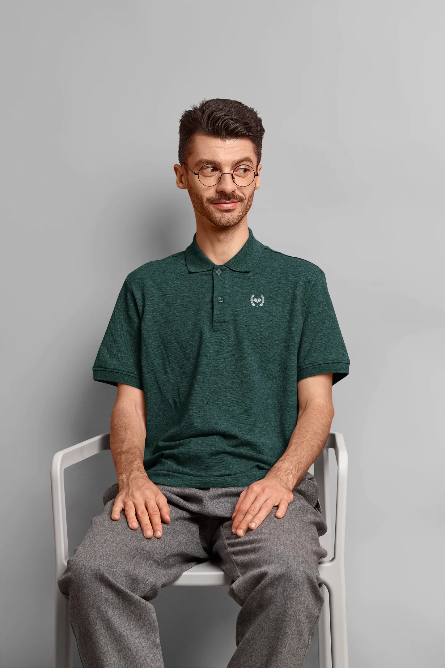 Man wearing a green polo shirt sitting on a chair against a gray background