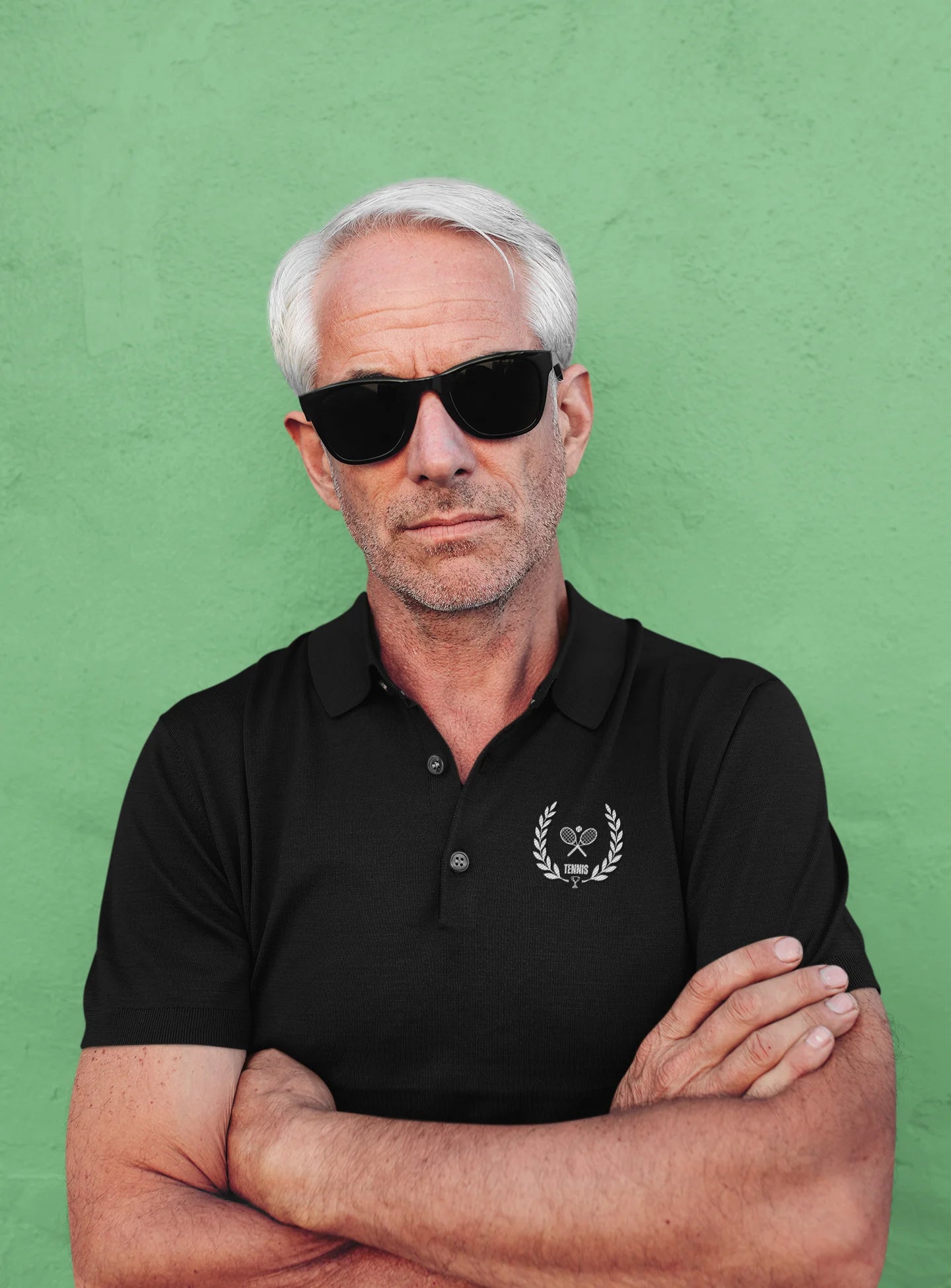 Man wearing sunglasses and a black polo shirt with a logo against a green background