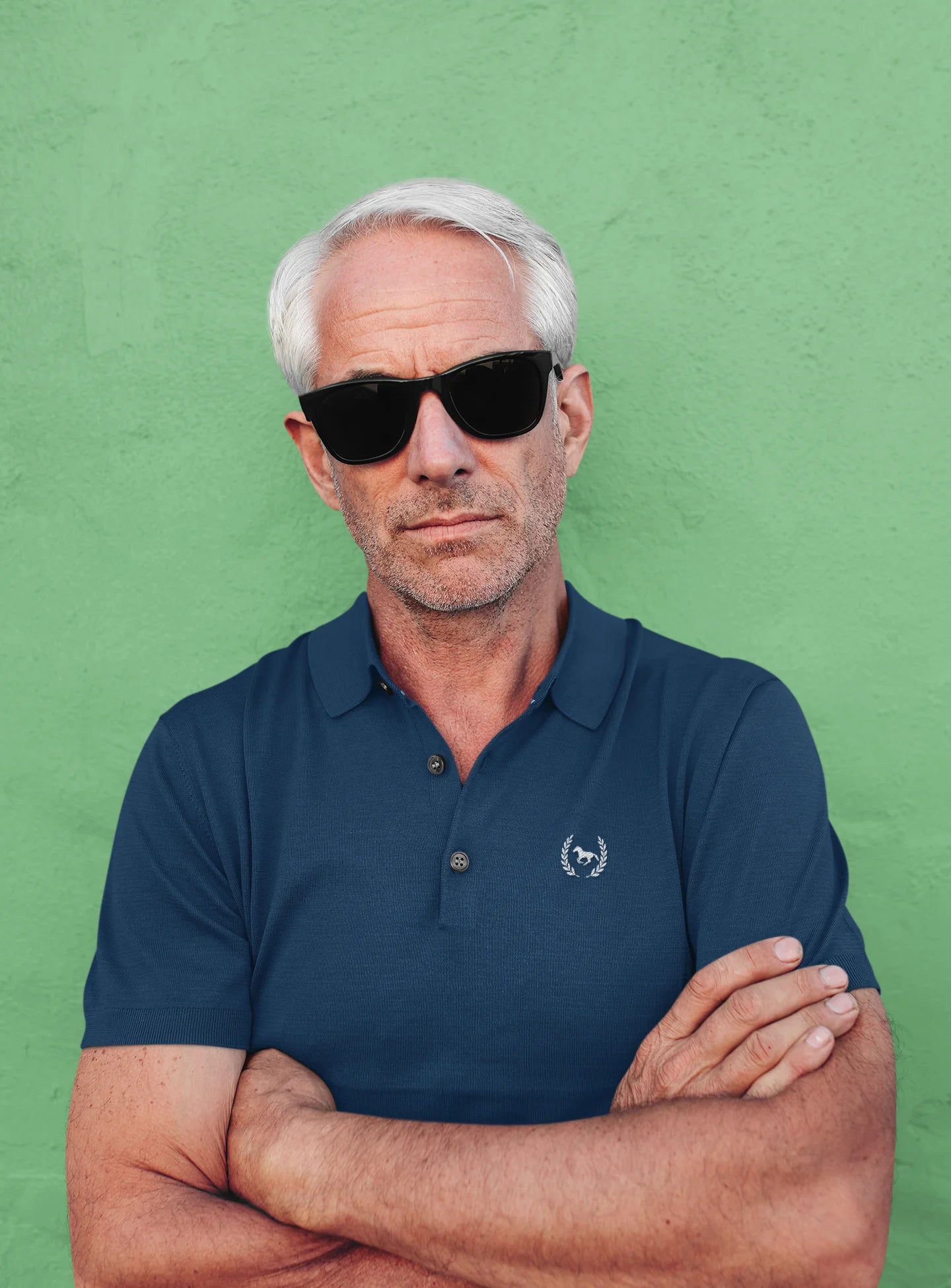Man wearing sunglasses and a navy polo shirt against a green background