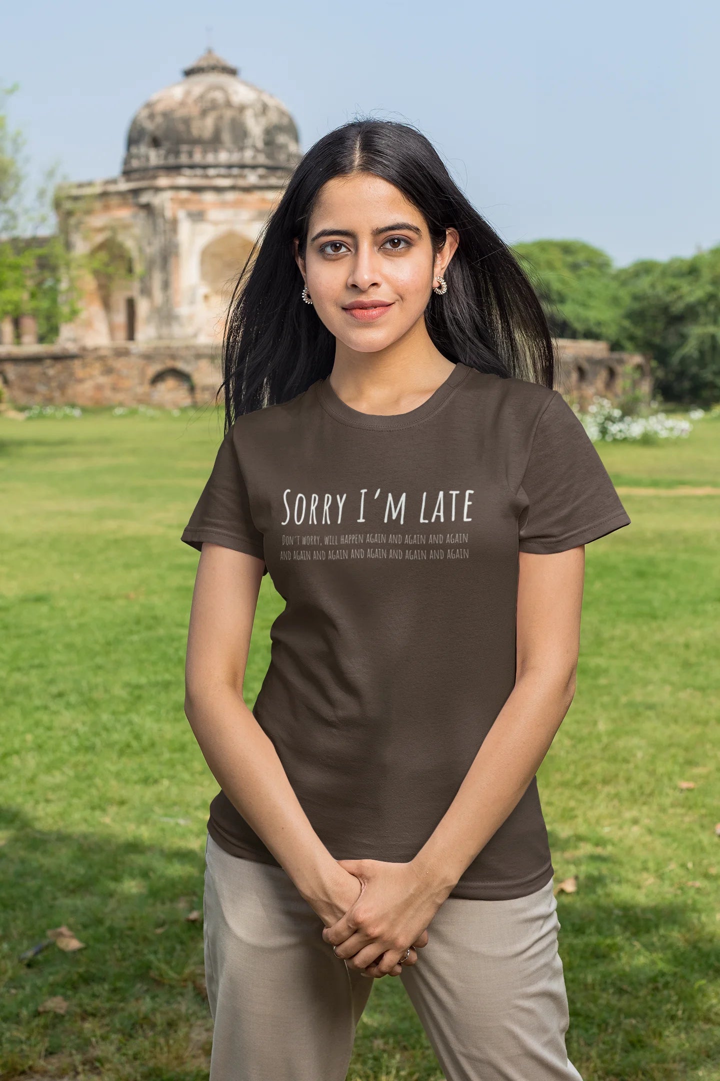 Woman wearing a brown t-shirt with 'Sorry I'm Late' text in an outdoor setting.