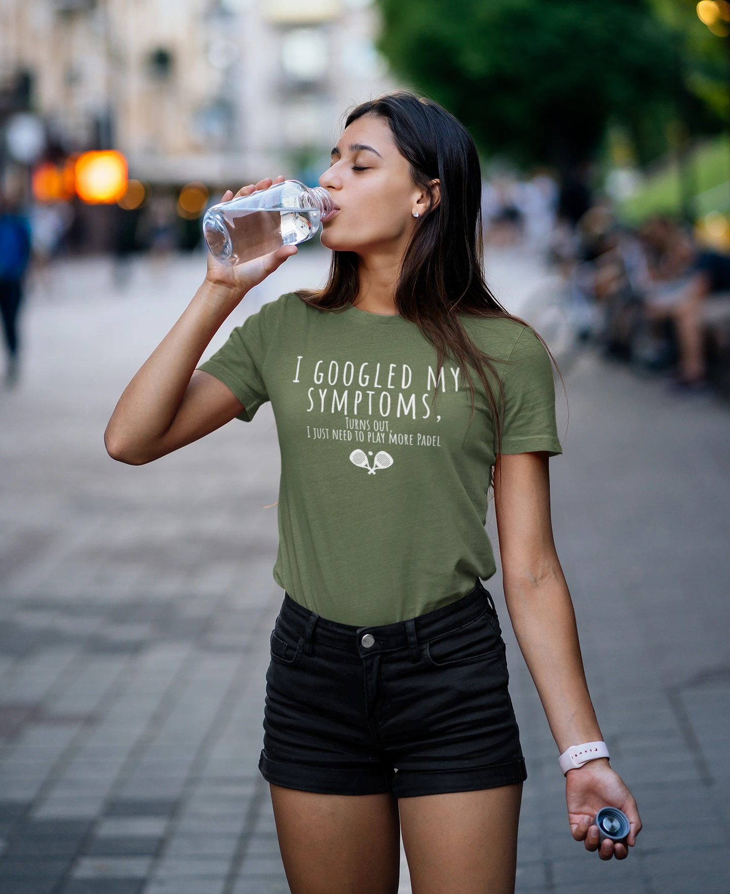 Woman drinking water outdoors wearing a green t-shirt with text.