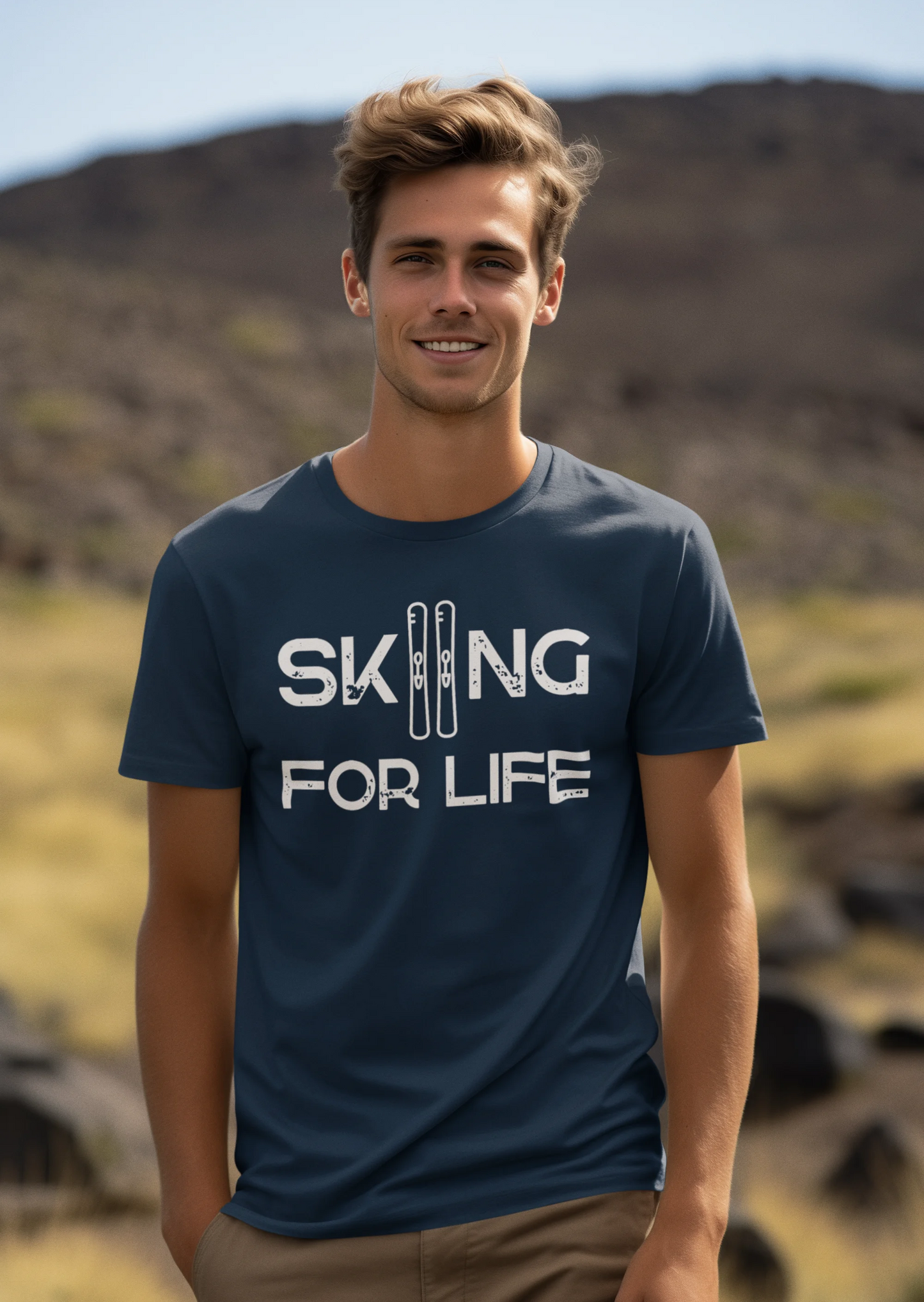 Man wearing a blue t-shirt with 'Skiing for Life' text in a mountainous landscape