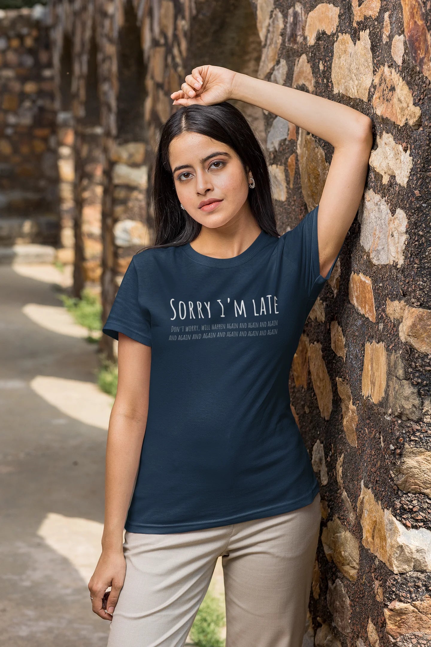 Woman wearing a navy blue t-shirt with text, leaning against a stone wall.