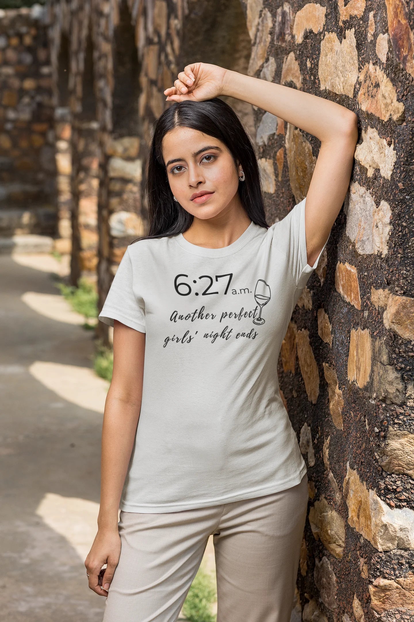 Woman wearing a t-shirt with text and a wine glass graphic against a stone wall.