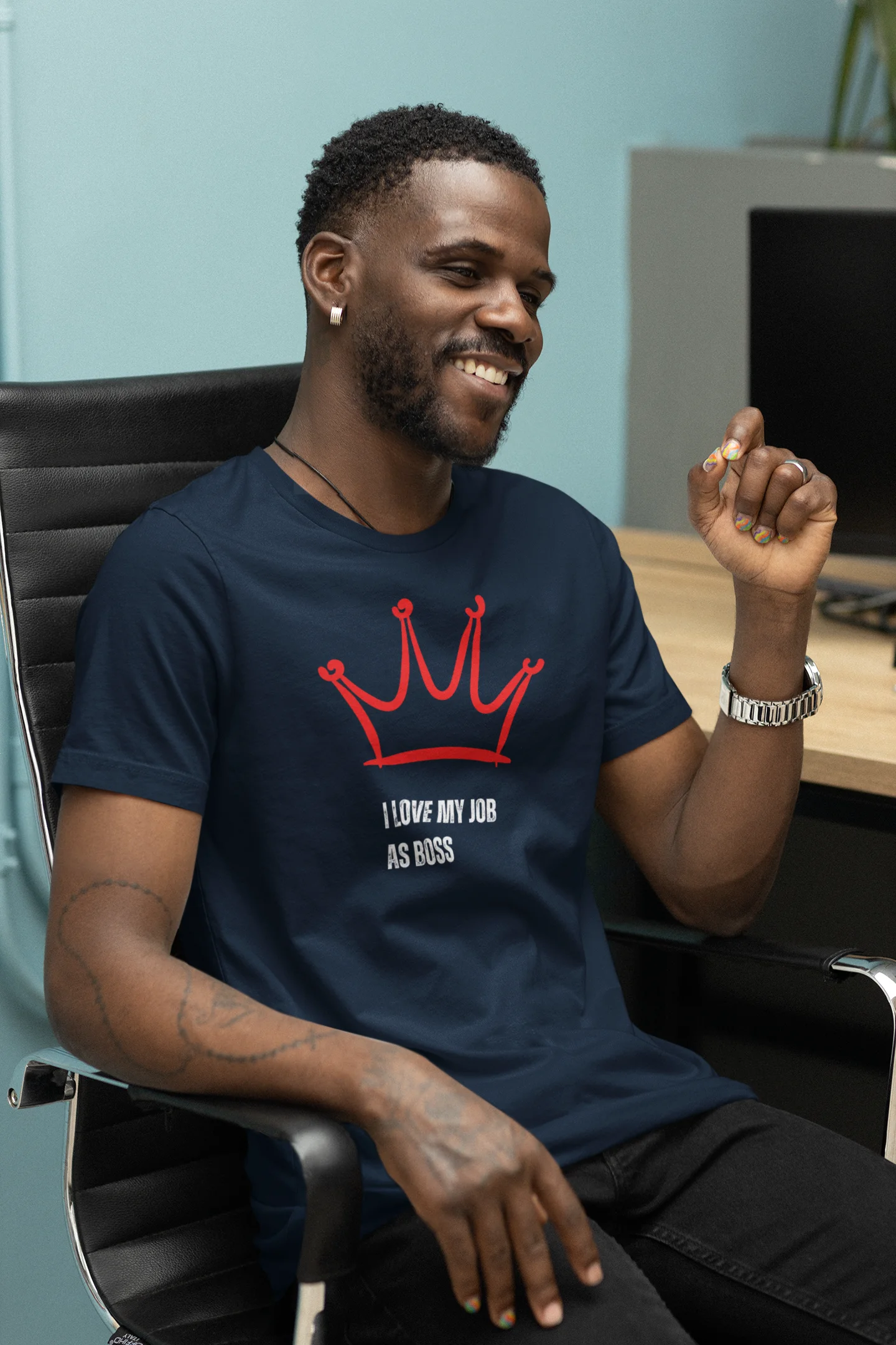 Gift for Boss Funny  Man wearing a navy blue t-shirt with a red crown design and text, sitting in an office chair.