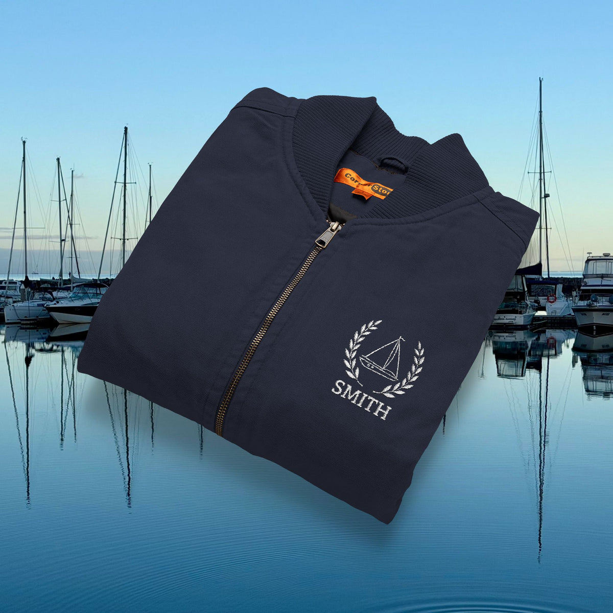 sailing vest A folded dark navy zip-up jacket with a white embroidered sailboat logo and the name 'SMITH' on the chest, shown over a marina background with boats and water reflections.