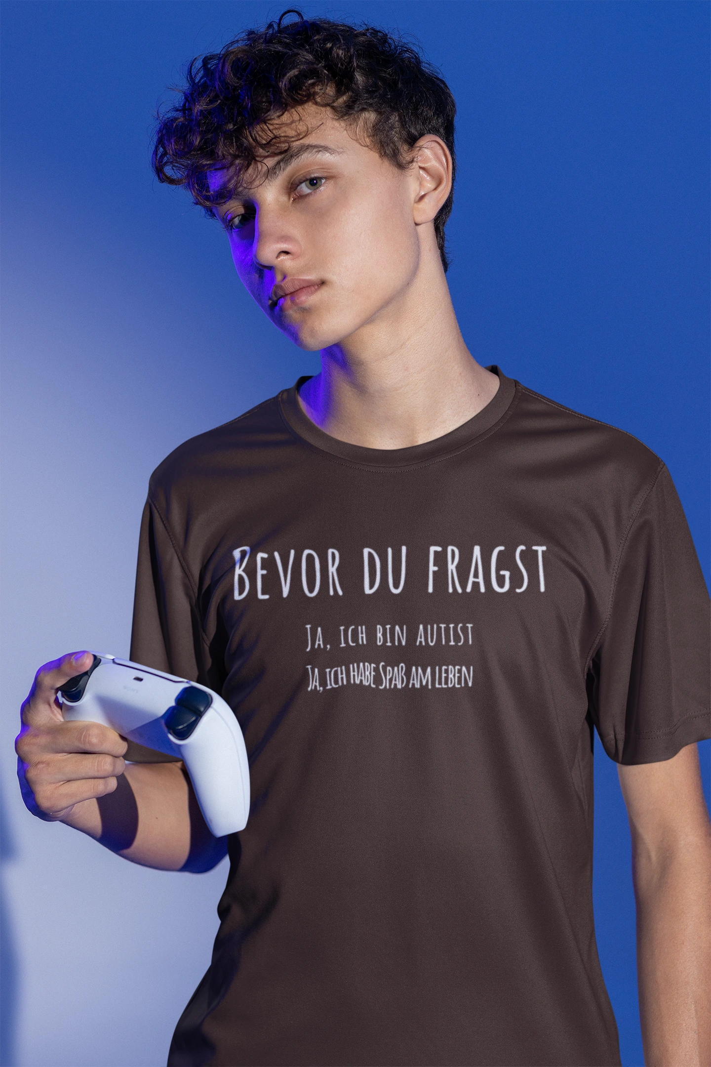 Person wearing a brown t-shirt with text, holding a gaming controller against a blue background