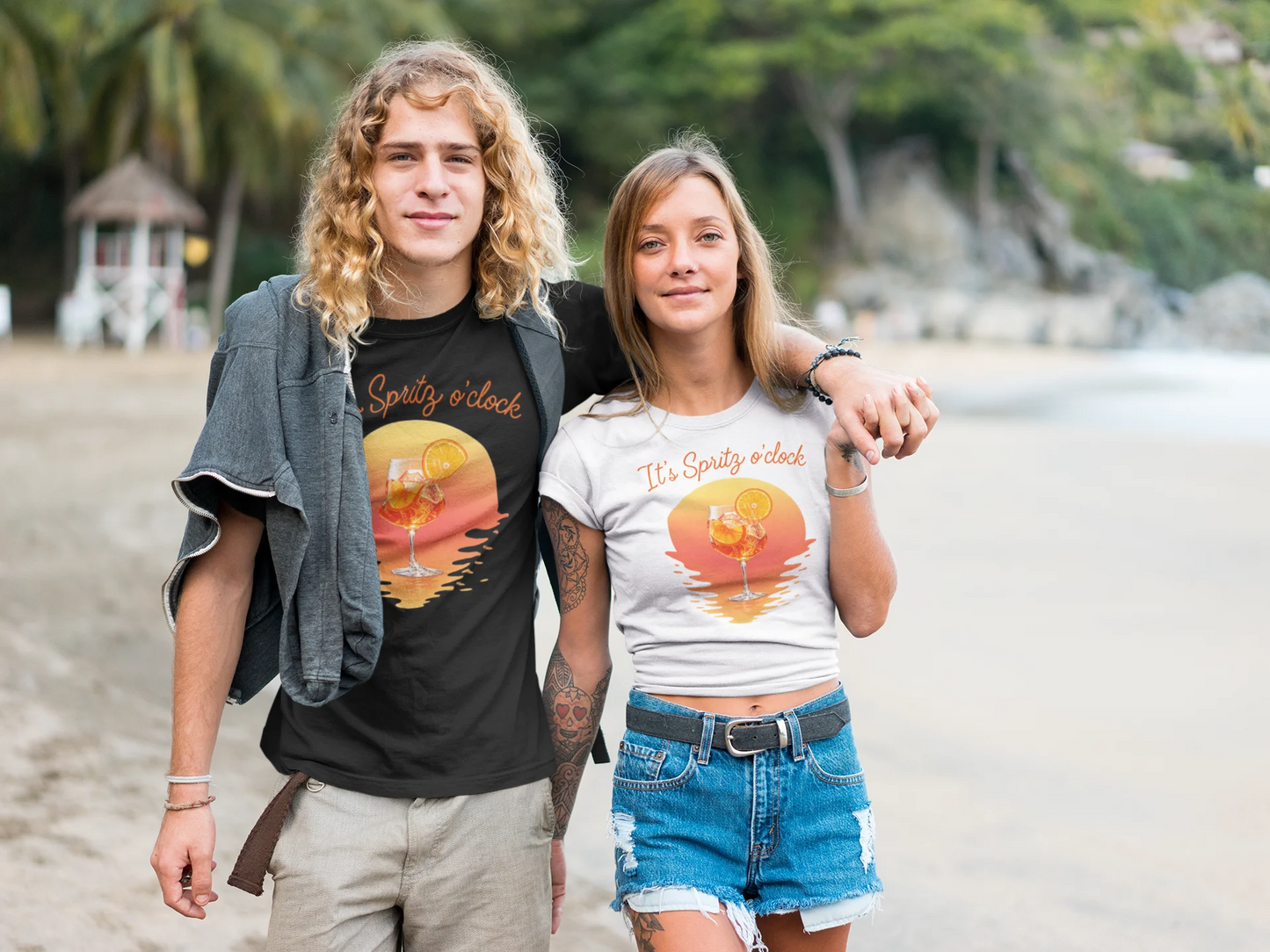 Aperol T-Shirt Two people standing on a beach wearing matching t-shirts with a sunset design.