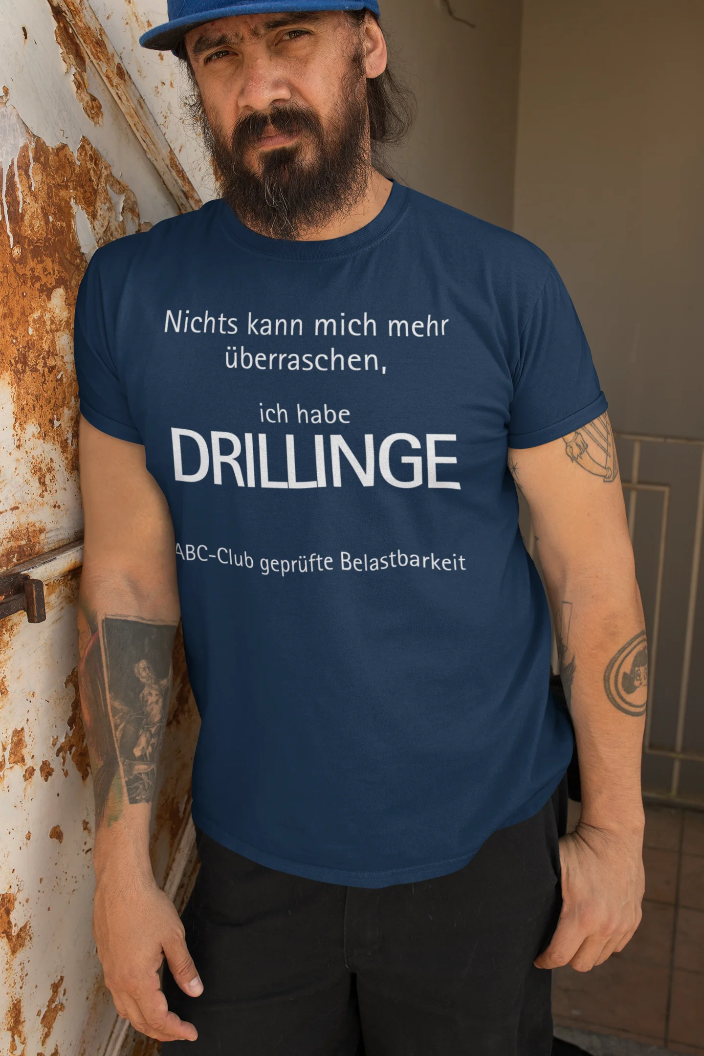 Geschenk für Drillinge Man wearing a blue t-shirt with German text standing against a wall.