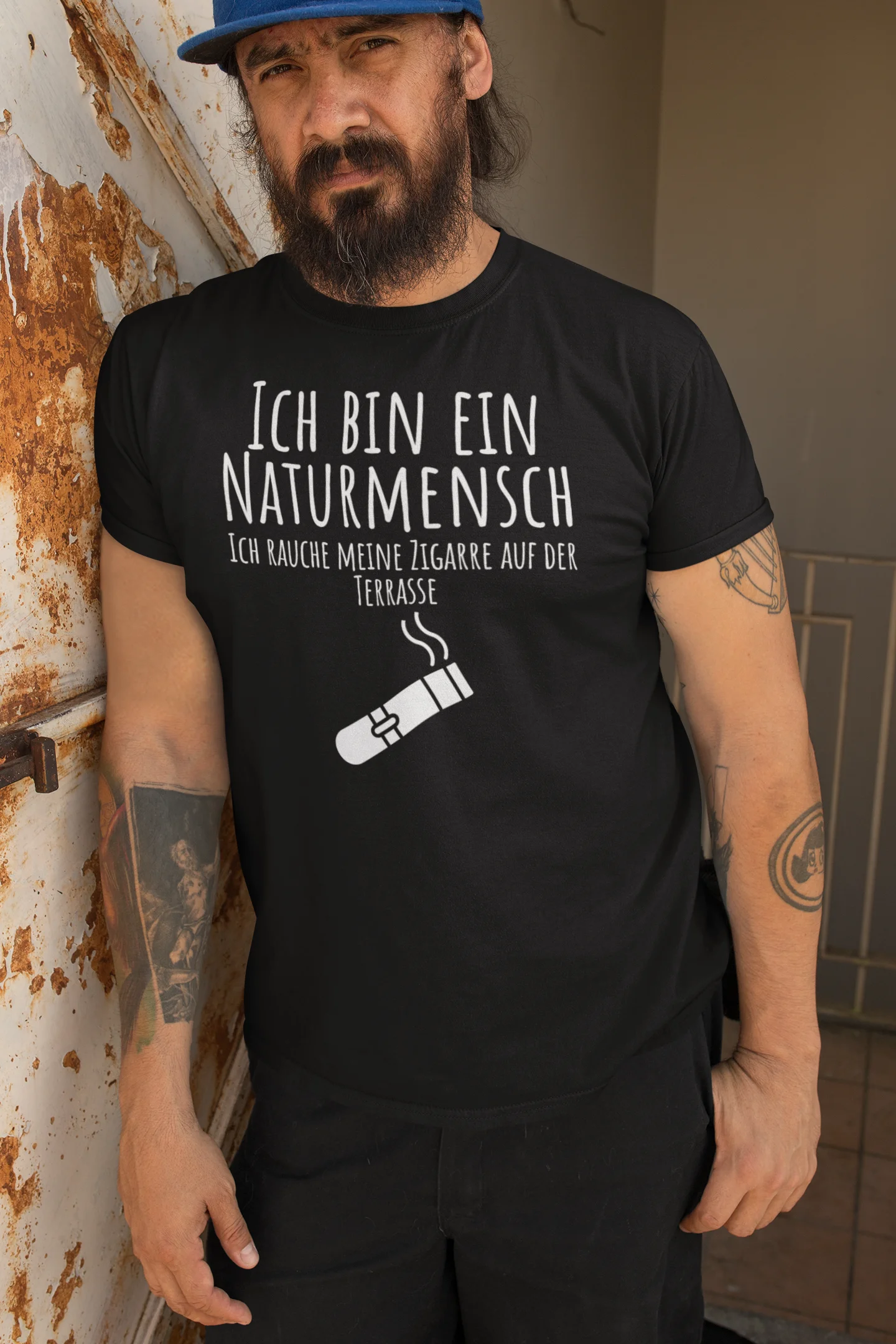 Man wearing a black t-shirt with white text and graphic, leaning against a wall.