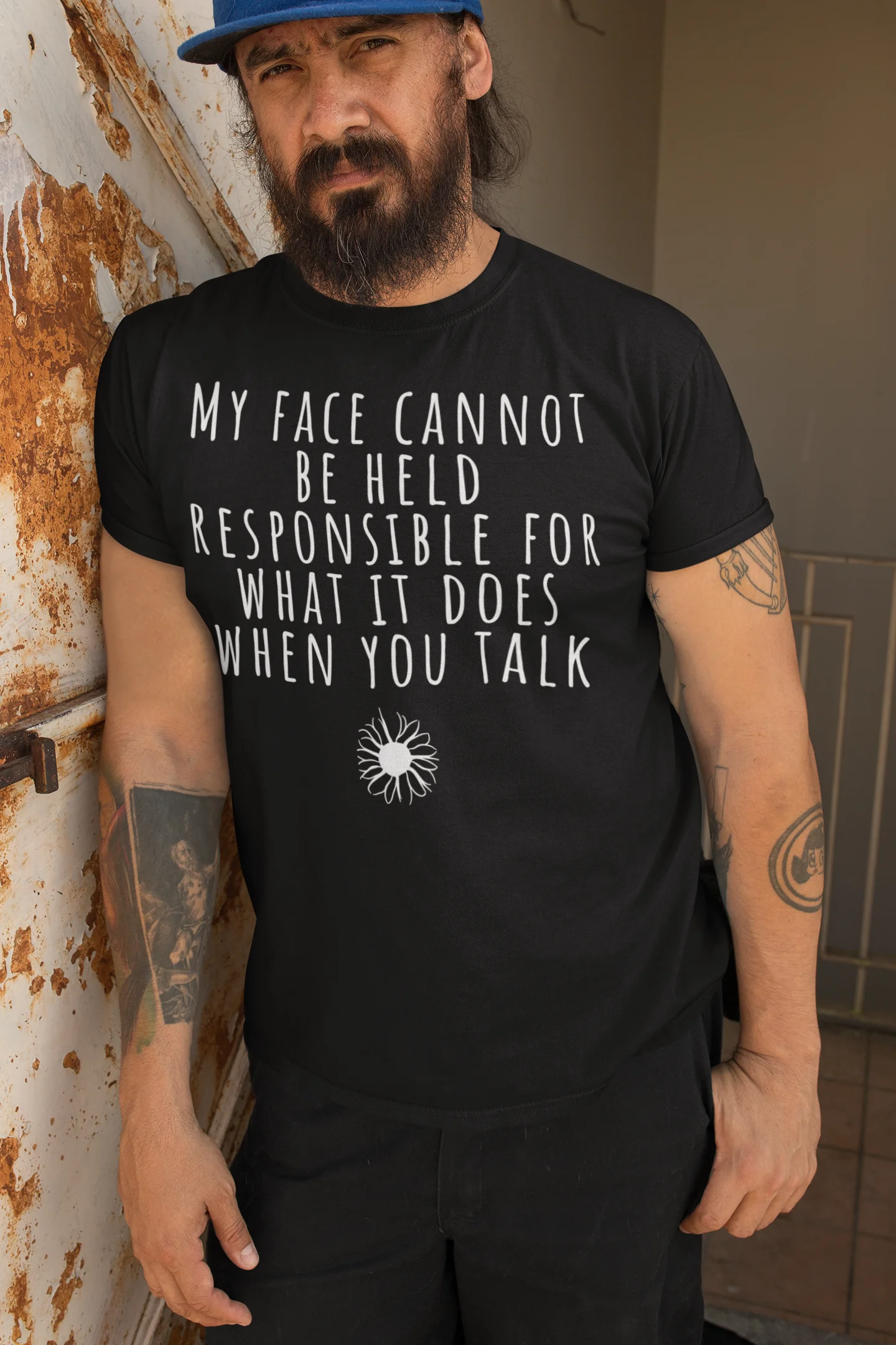 Man wearing a black t-shirt with text and a graphic, standing against a wall.