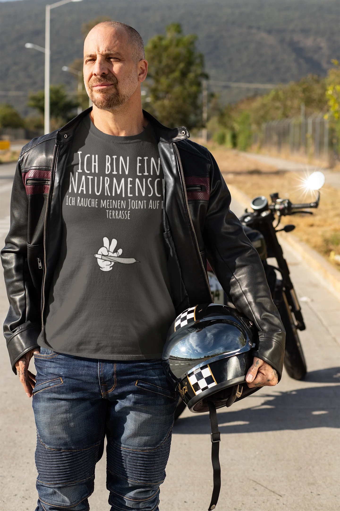 Man in leather jacket holding a helmet with a motorcycle in the background
