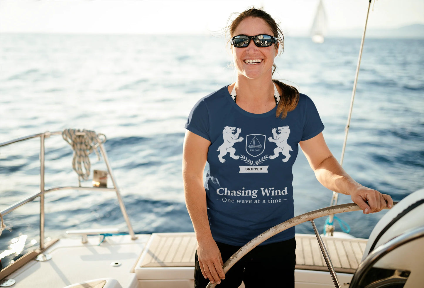 Sailing Boat T Shirt Woman on a sailboat wearing a navy blue t-shirt with a logo and text.