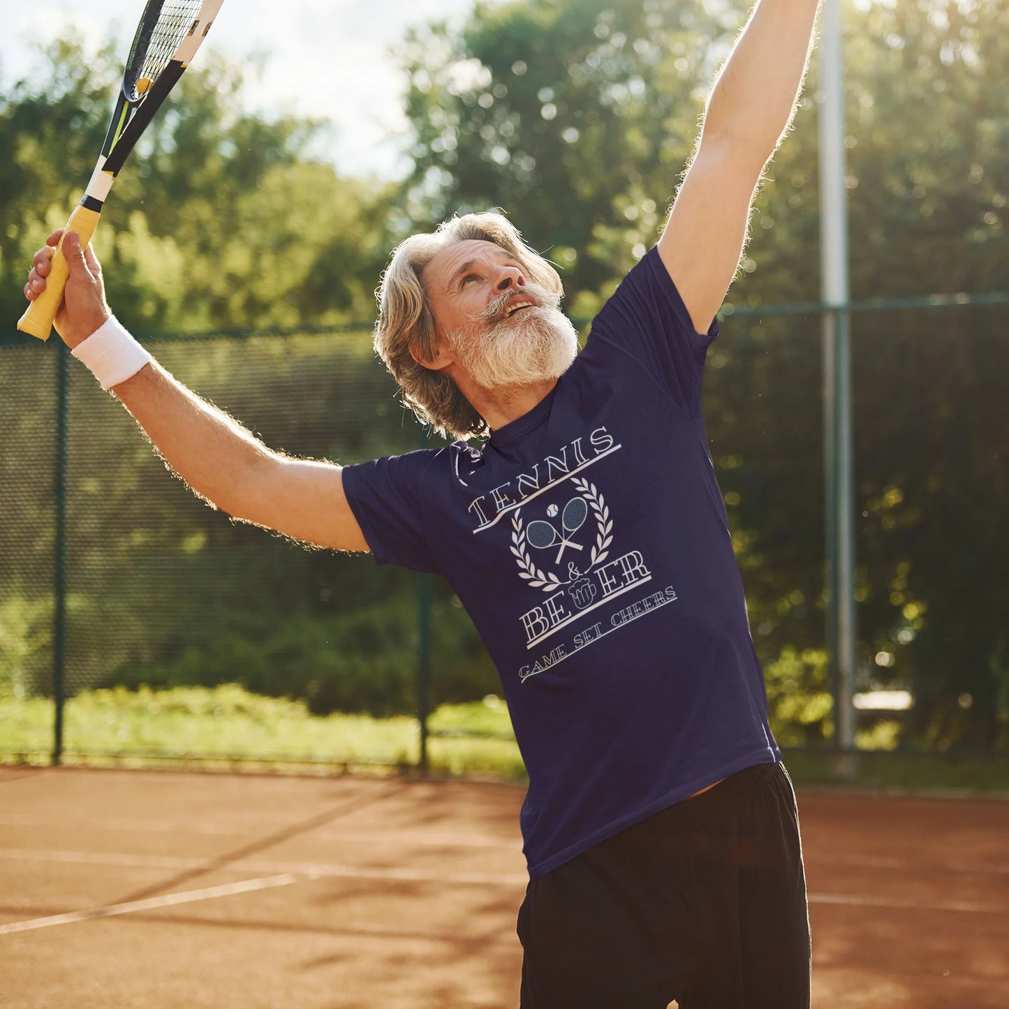 Man playing tennis on a court with trees in the background