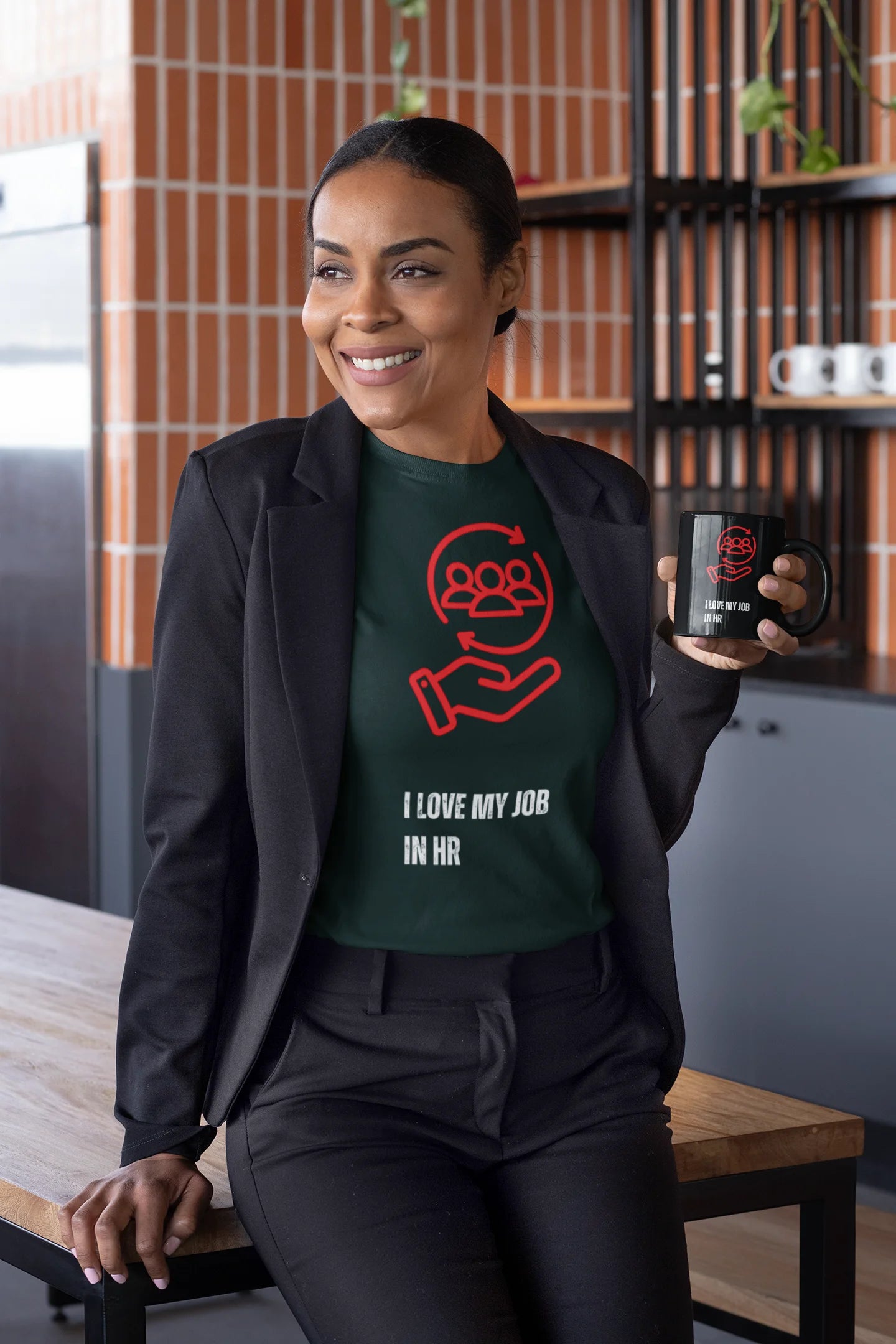 I love my Job T-Shirt Woman wearing a green t-shirt with a red graphic and text, holding a black mug in a kitchen setting.