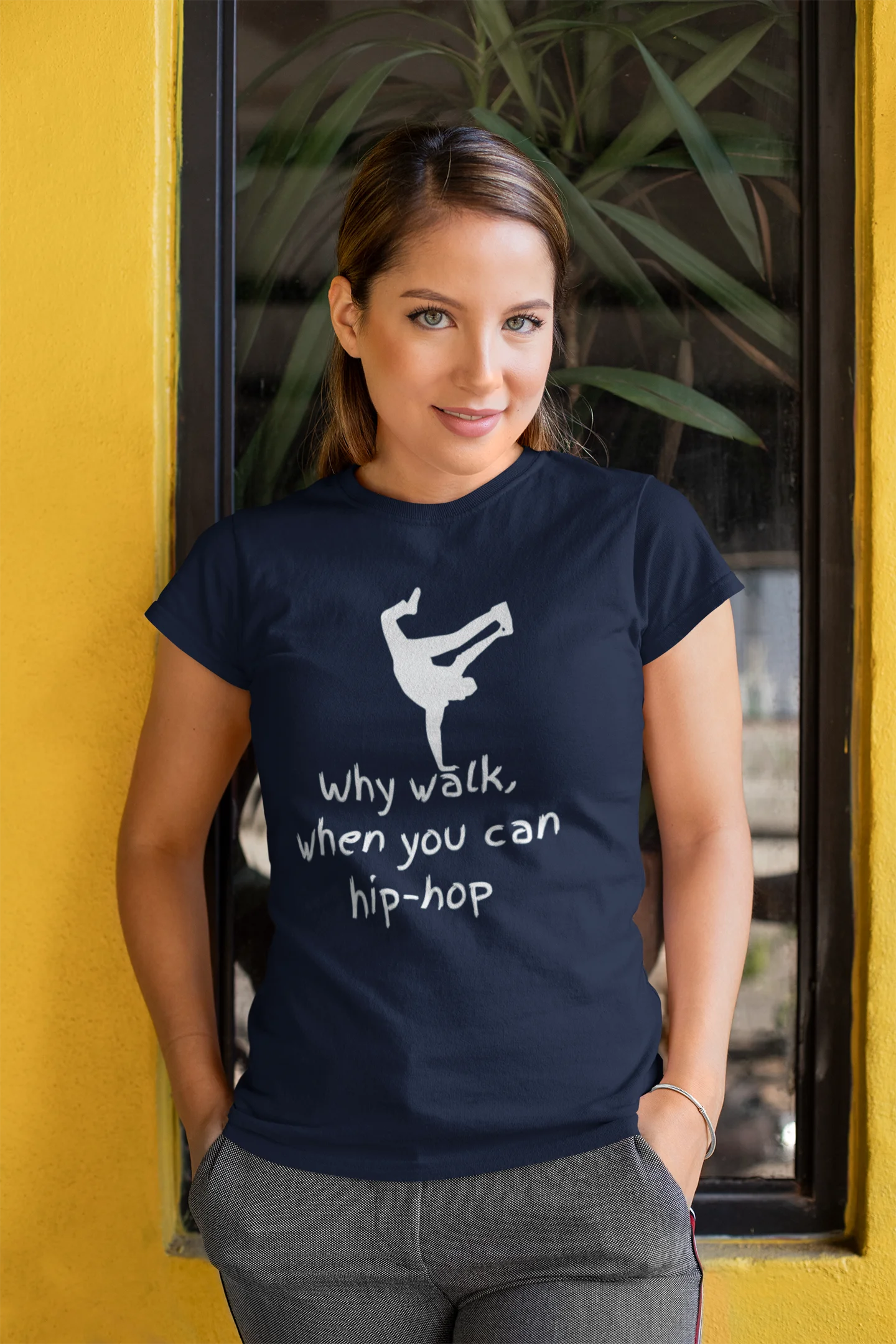 Woman wearing a navy blue t-shirt with a white graphic and text, standing against a yellow wall.