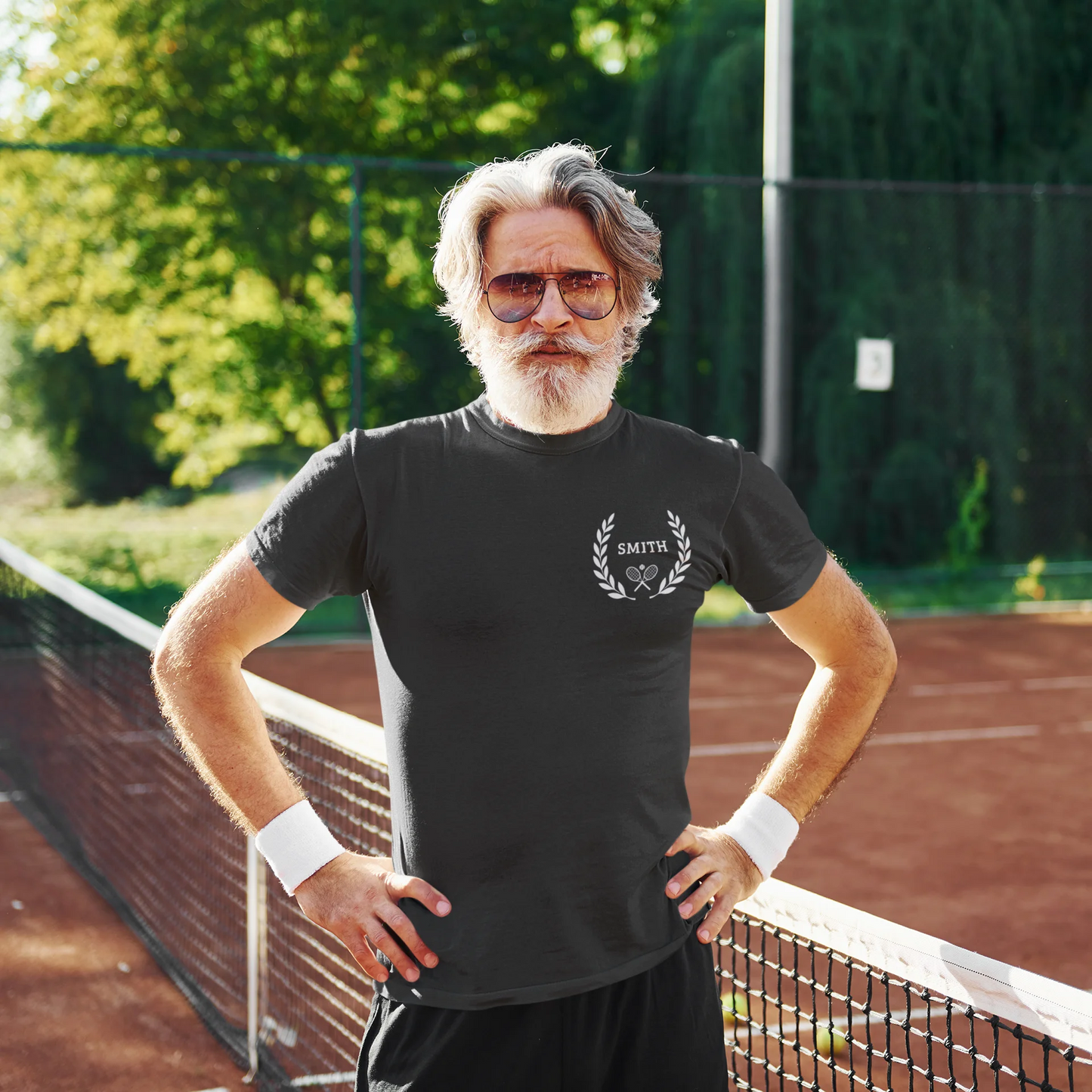 Unique gifts for tennis players Man standing on a tennis court wearing a black t-shirt with a logo, sunglasses, and wristbands.