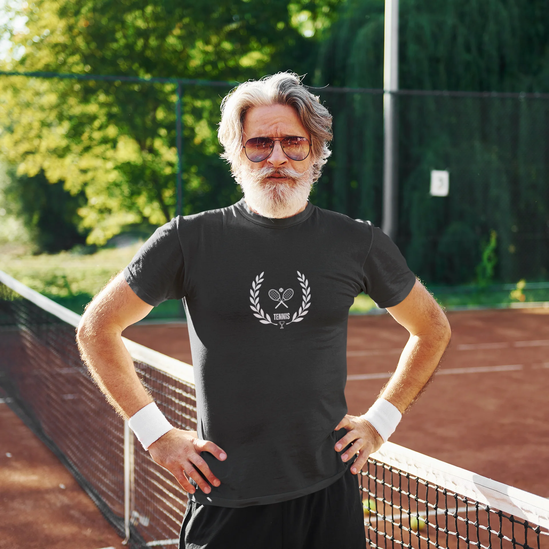 Man on a tennis court wearing a black t-shirt with a logo, sunglasses, and wristbands.