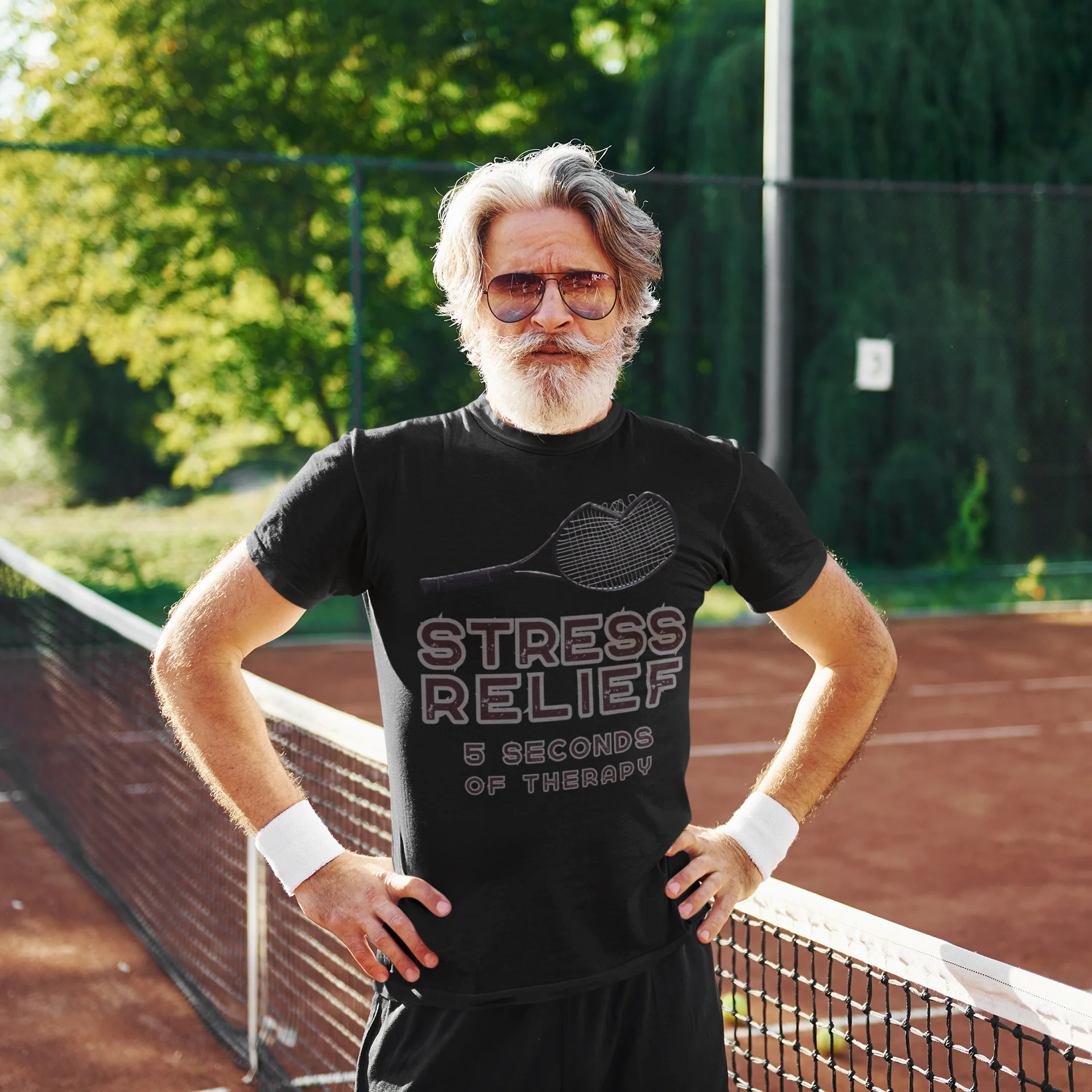 Man on a tennis court wearing a black t-shirt with text, standing with hands on hips.