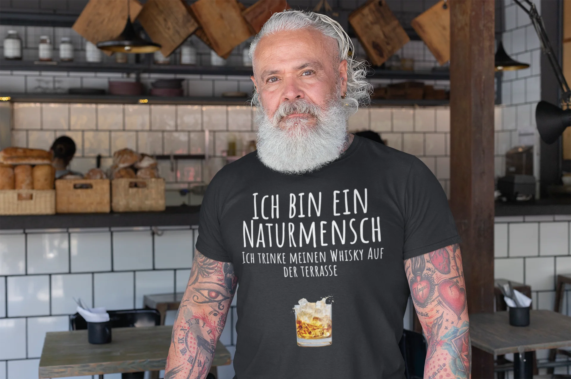 Naturmensch Whisky auf der Terrasse Man with tattoos wearing a black t-shirt with German text in a restaurant setting