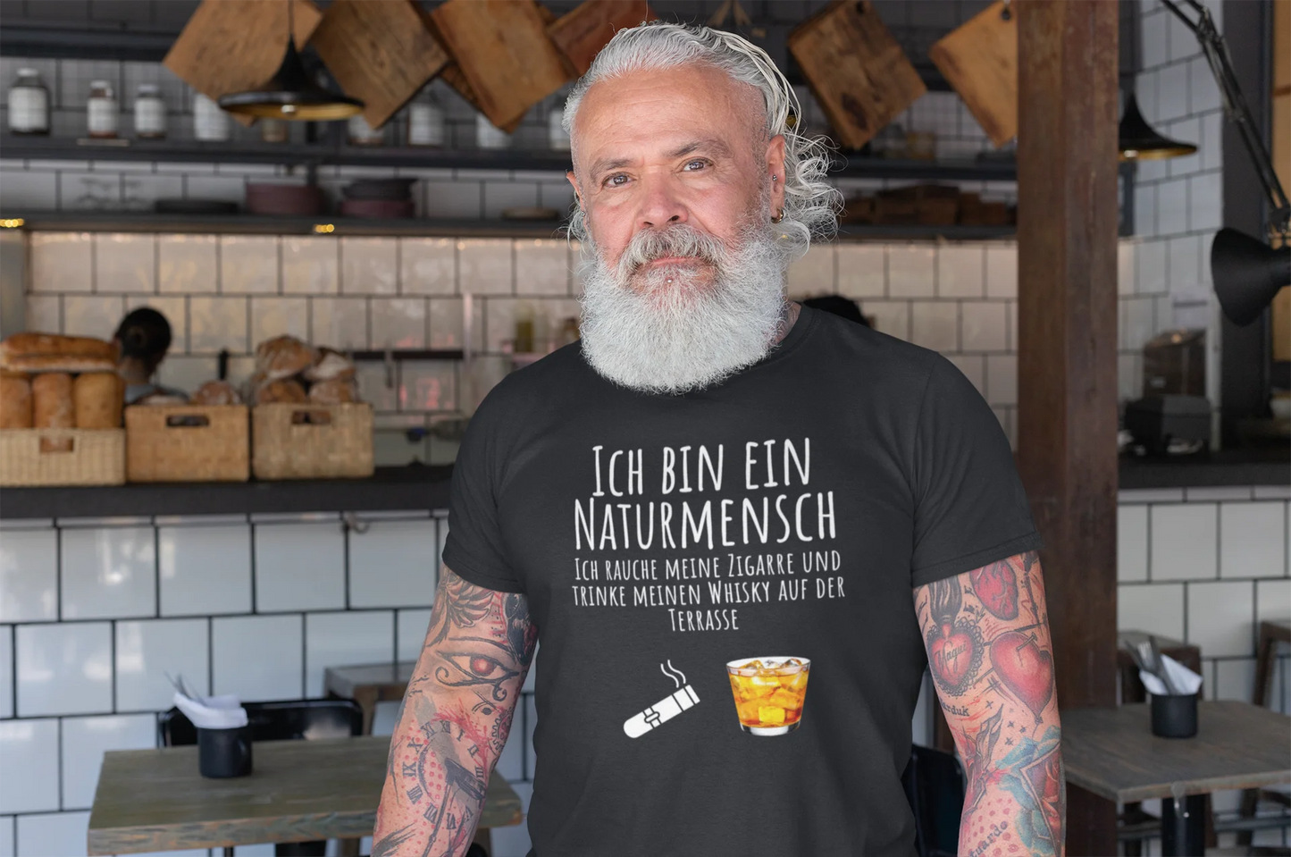 Man with tattoos wearing a black t-shirt with German text in a kitchen setting
