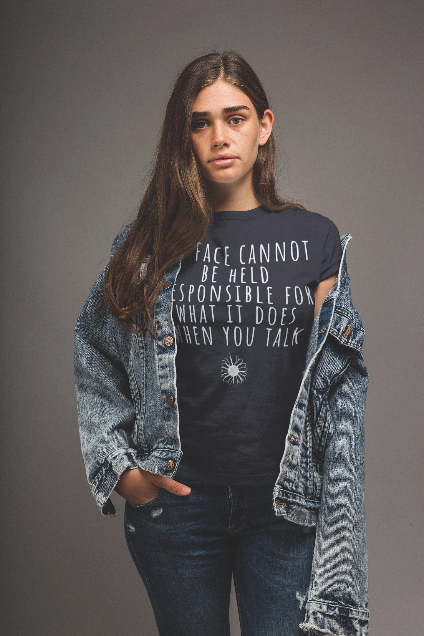 Person wearing a black t-shirt with text and a denim jacket on a gray background
