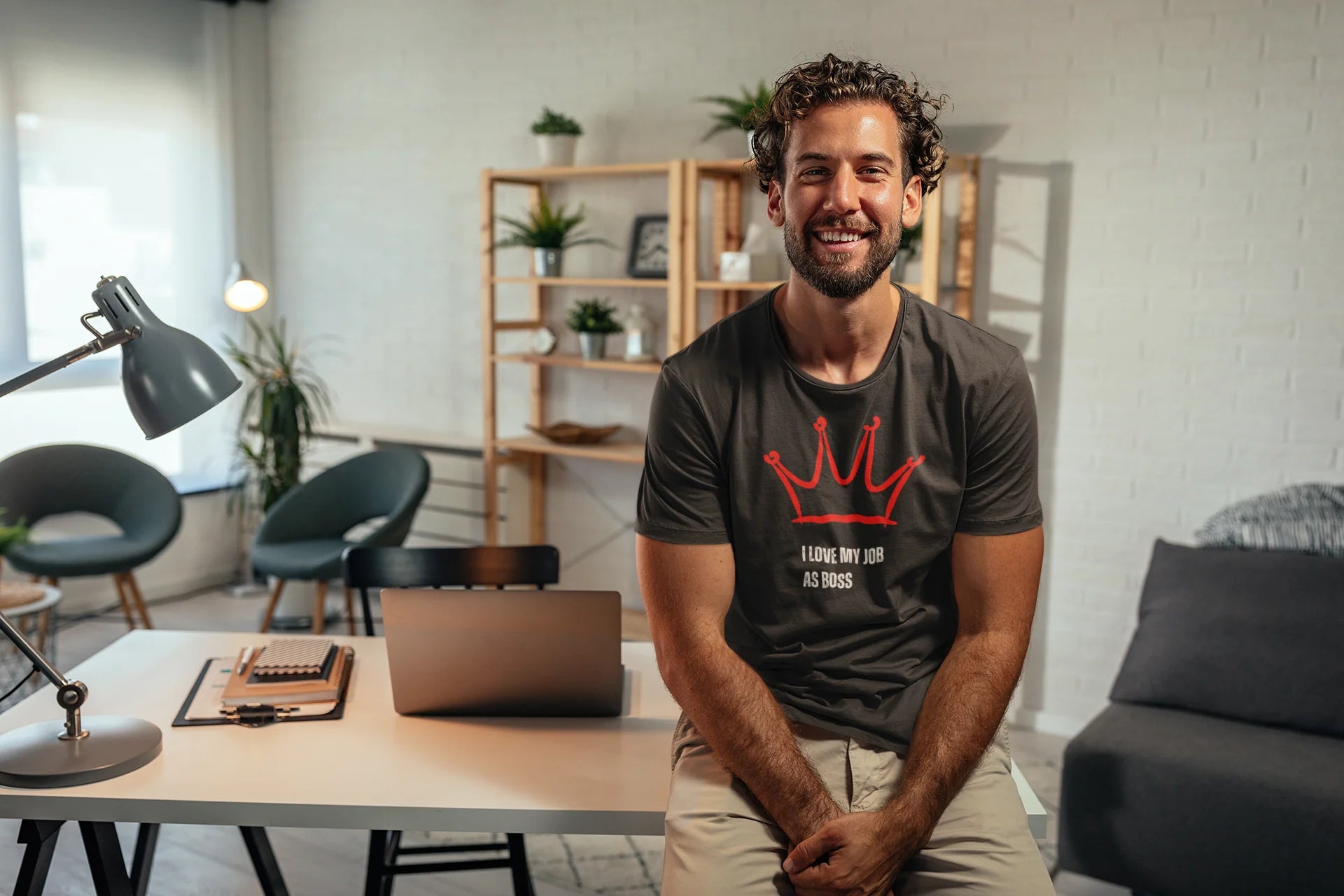 Gift for Boss Funny  Man sitting at a desk in a modern office setting wearing a black t-shirt with a red logo and text.