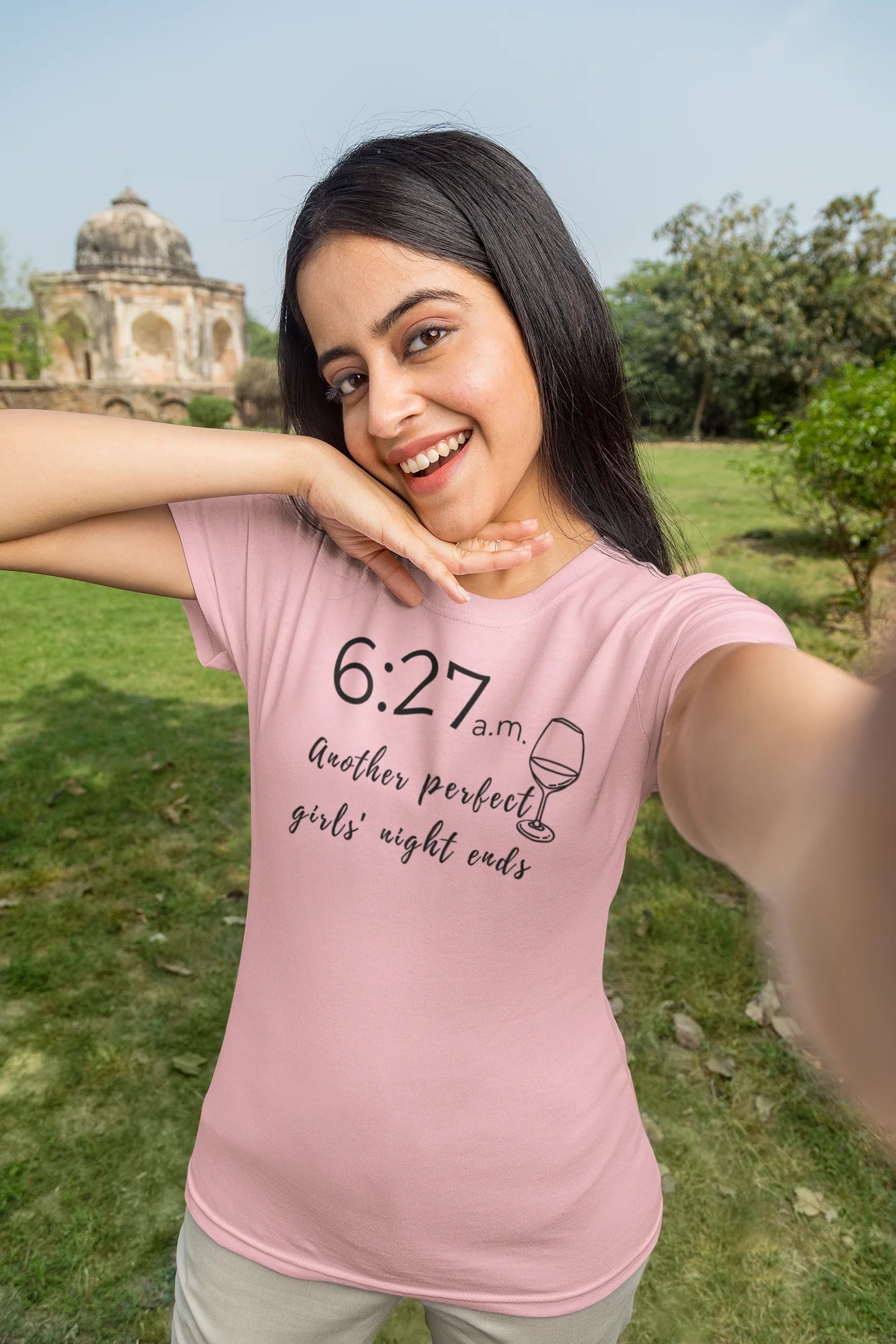 Woman wearing a pink t-shirt with text and a graphic, standing outdoors.