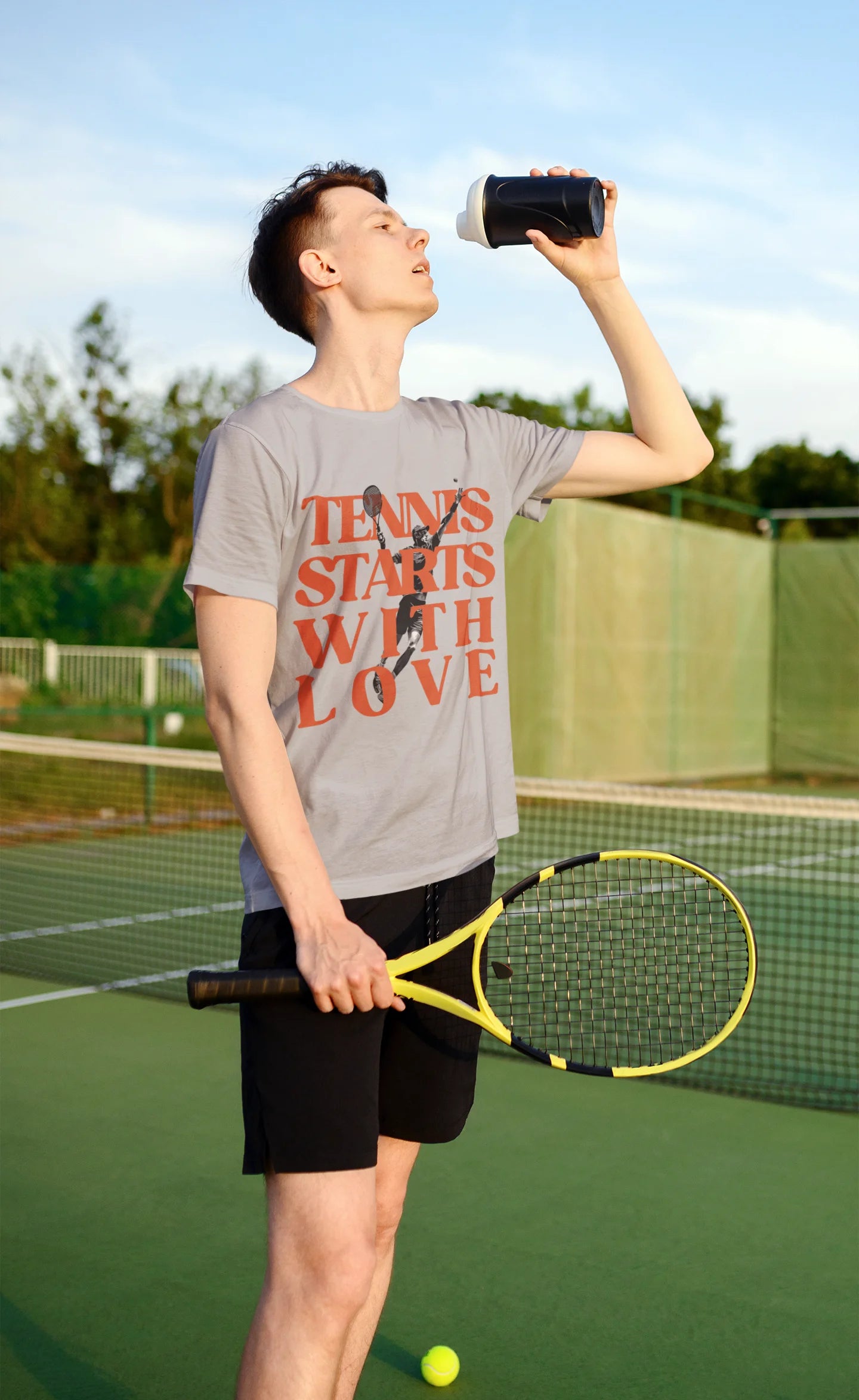Tennis lover Shirt Person on a tennis court holding a racket and drinking from a bottle, with 'Tennis Starts With Love' t-shirt.
