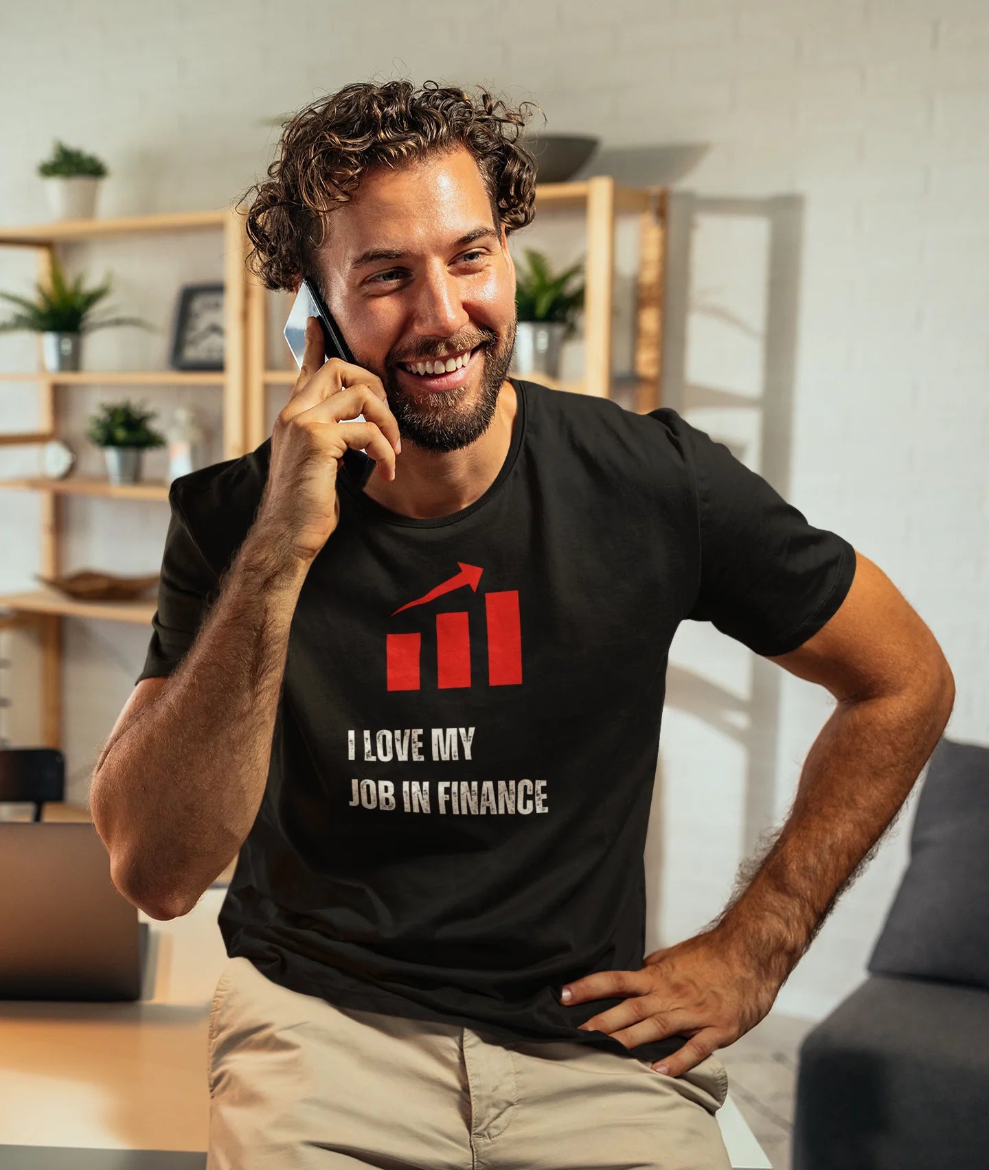 Finance Manager Shirt Man wearing a black t-shirt with a graphic and text, sitting indoors.