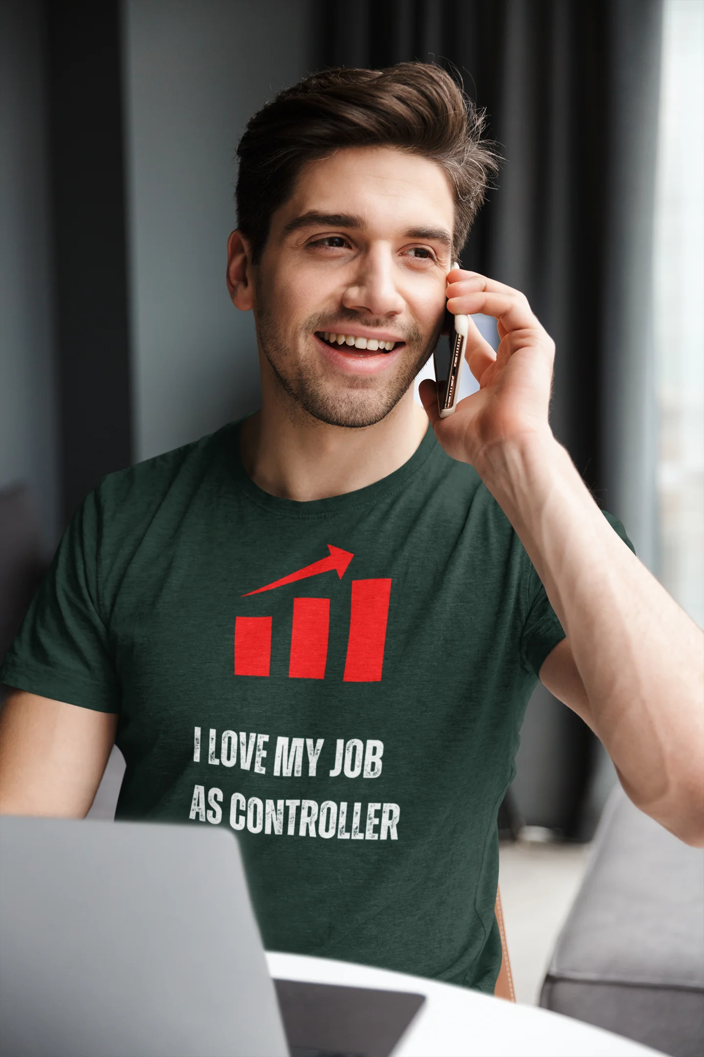 Finance Controller Shirt Man wearing a green t-shirt with a graphic and text, talking on a phone indoors.