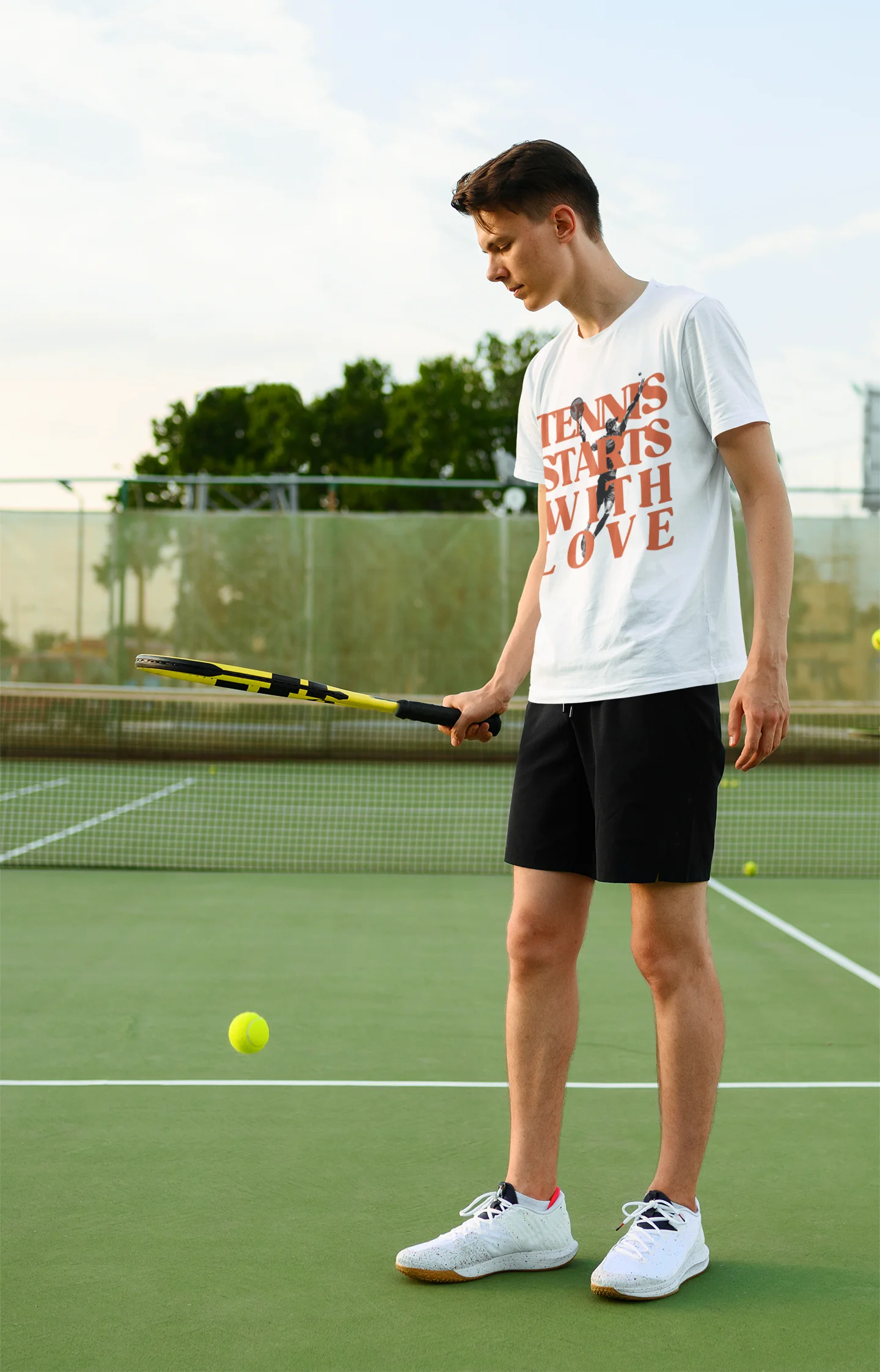 Tennis lover Shirt Person on a tennis court holding a racket and a tennis ball, wearing a white t-shirt with text and black shorts.