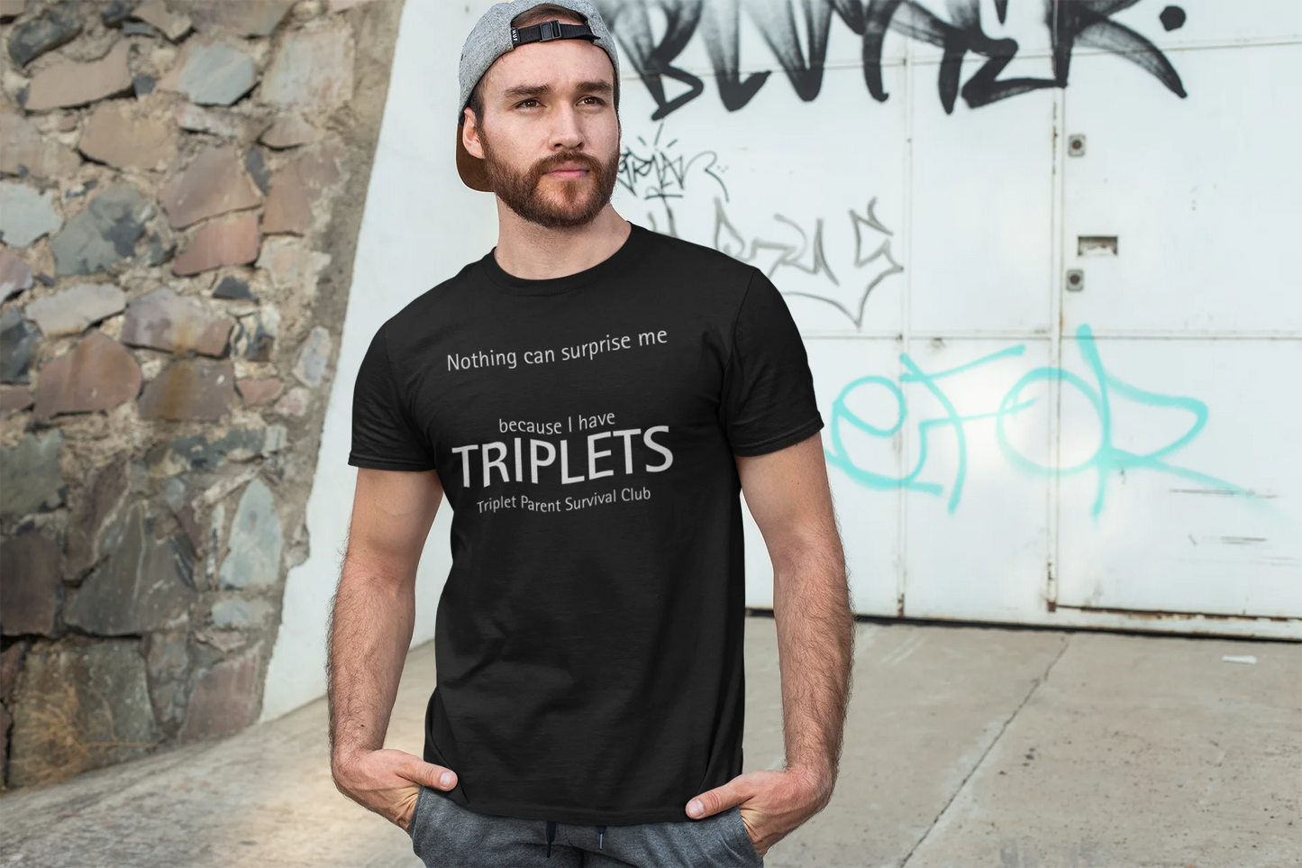 Man wearing a black t-shirt with text standing in front of a graffiti-covered wall.