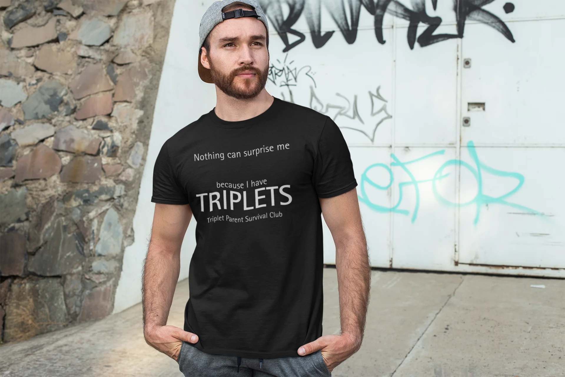 Man wearing a black t-shirt with text standing in front of a graffiti-covered wall.