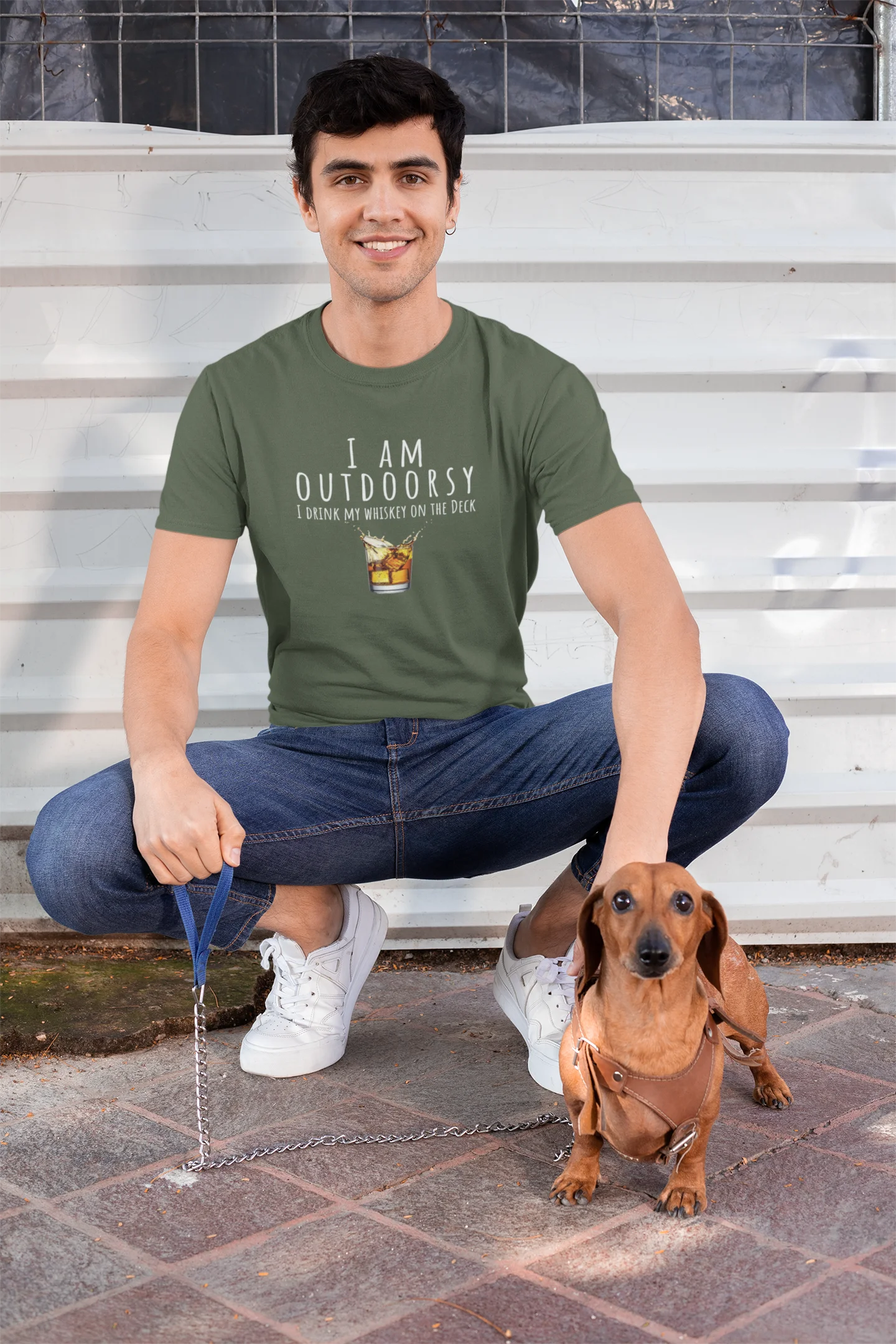 Man wearing a green t-shirt with 'I AM OUTDOORSY' text, sitting on steps with a small dog.