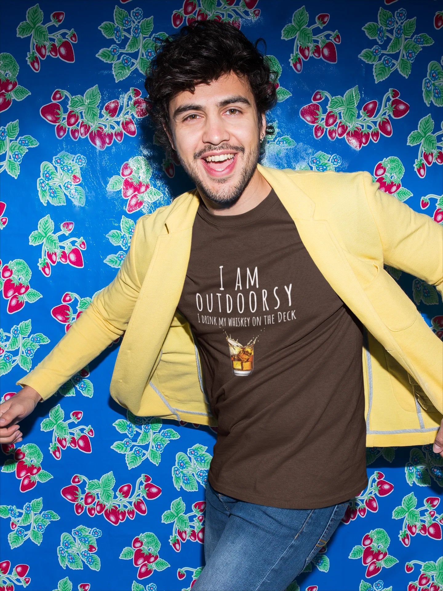 Person wearing a yellow jacket over a brown t-shirt with text, standing against a colorful floral-patterned background.