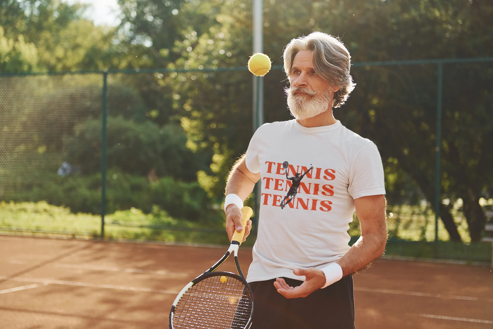 Man on a tennis court with a racket and ball, wearing a t-shirt with 'Tennis Tennis Tennis' text.