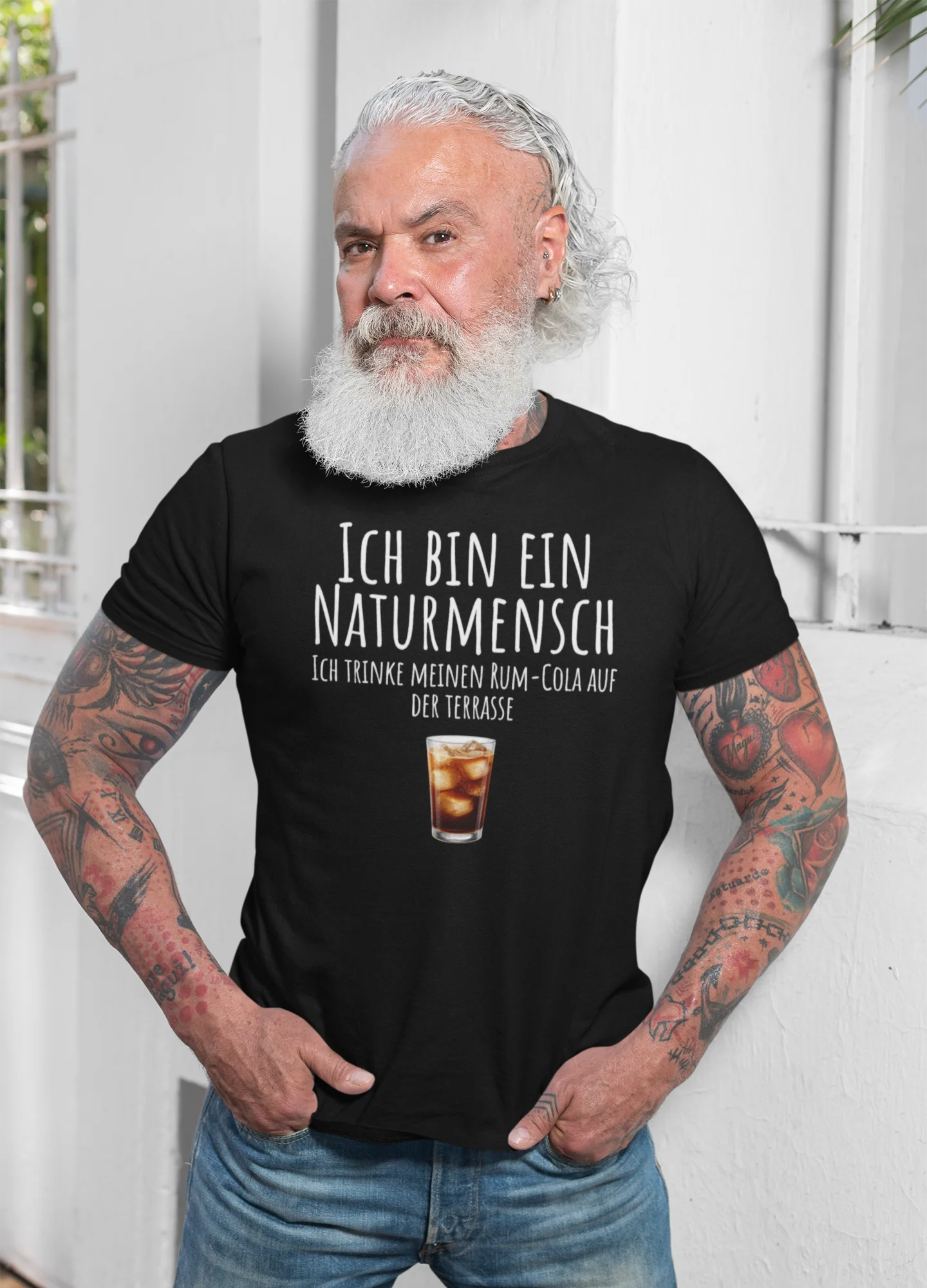 Man wearing a black t-shirt with German text and a drink graphic, standing against a white wall.