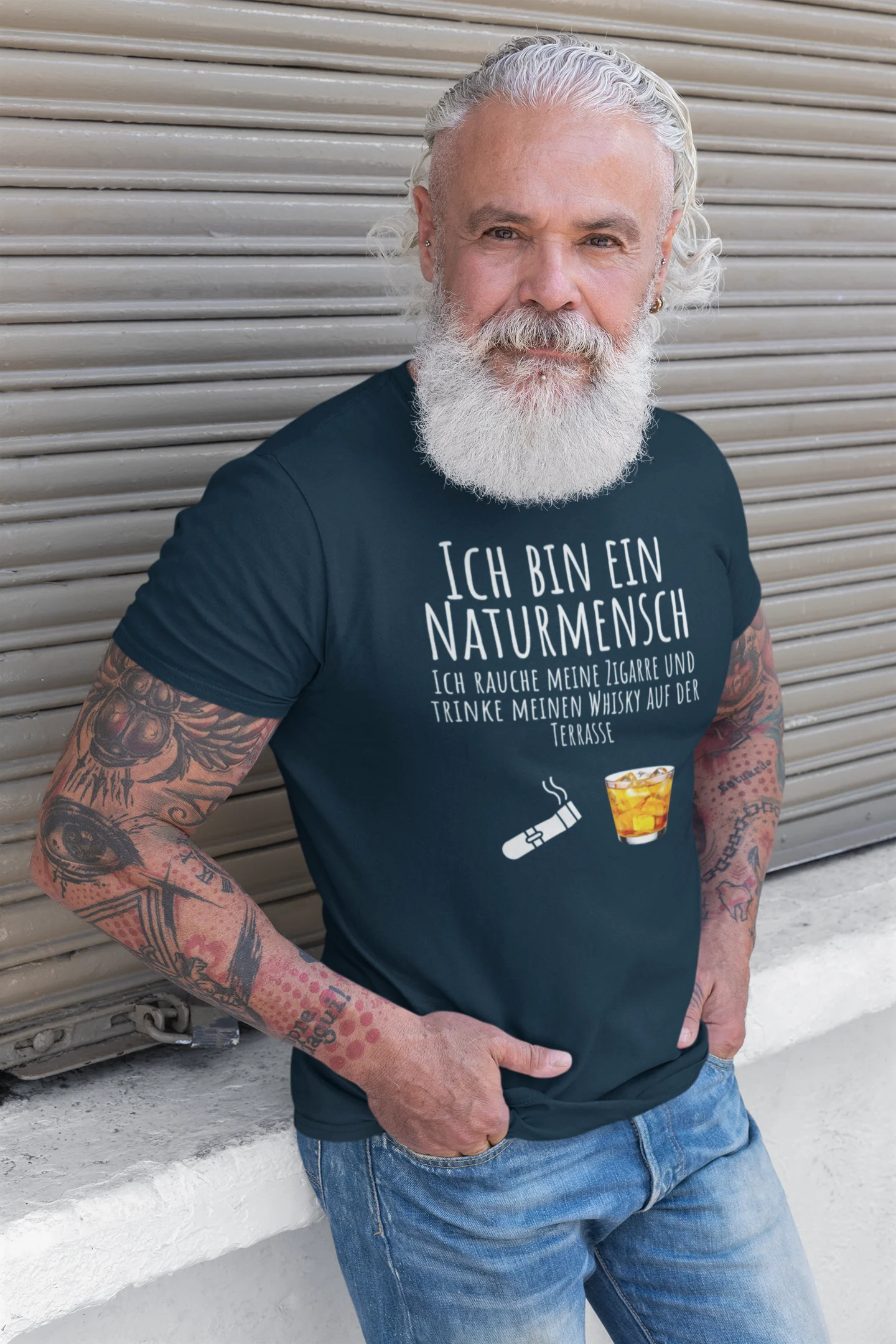 Man wearing a black t-shirt with German text and a graphic, standing in front of a metallic shutter.