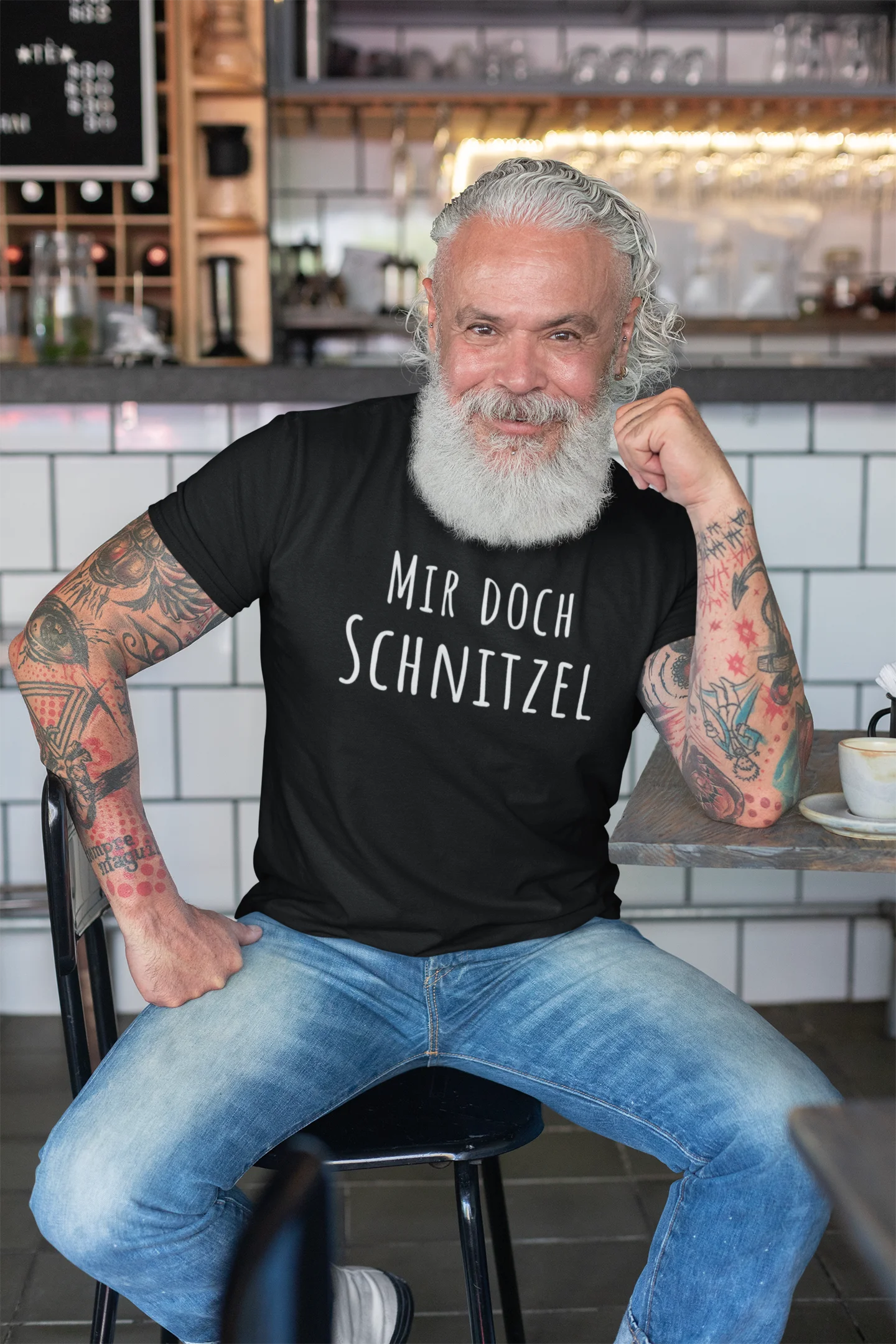 Man with tattoos and a beard wearing a black t-shirt with text in a casual setting.
