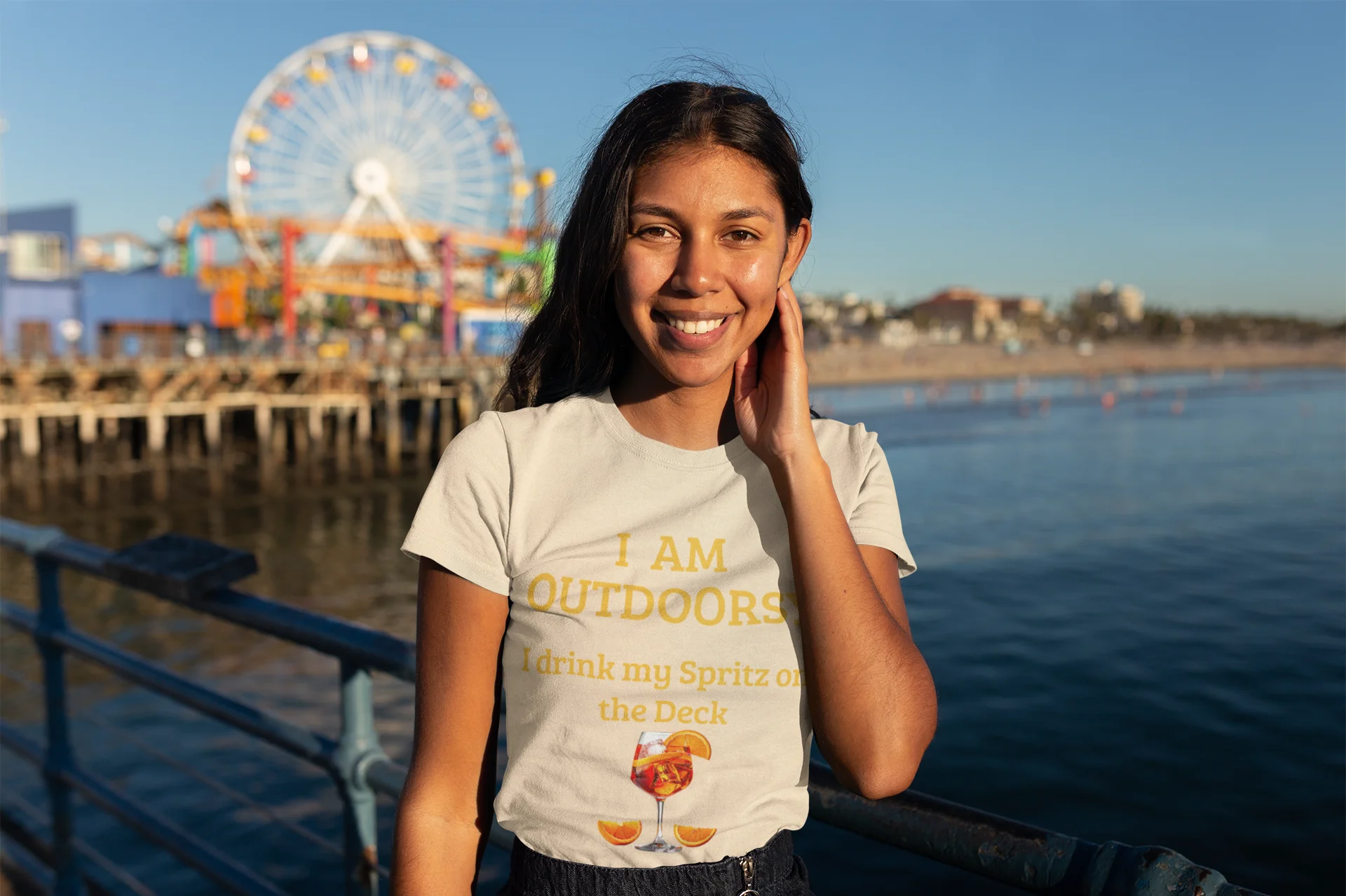 Funny Spritz Shirt Woman wearing a t-shirt with text and graphics, standing by a waterfront with a Ferris wheel in the background.