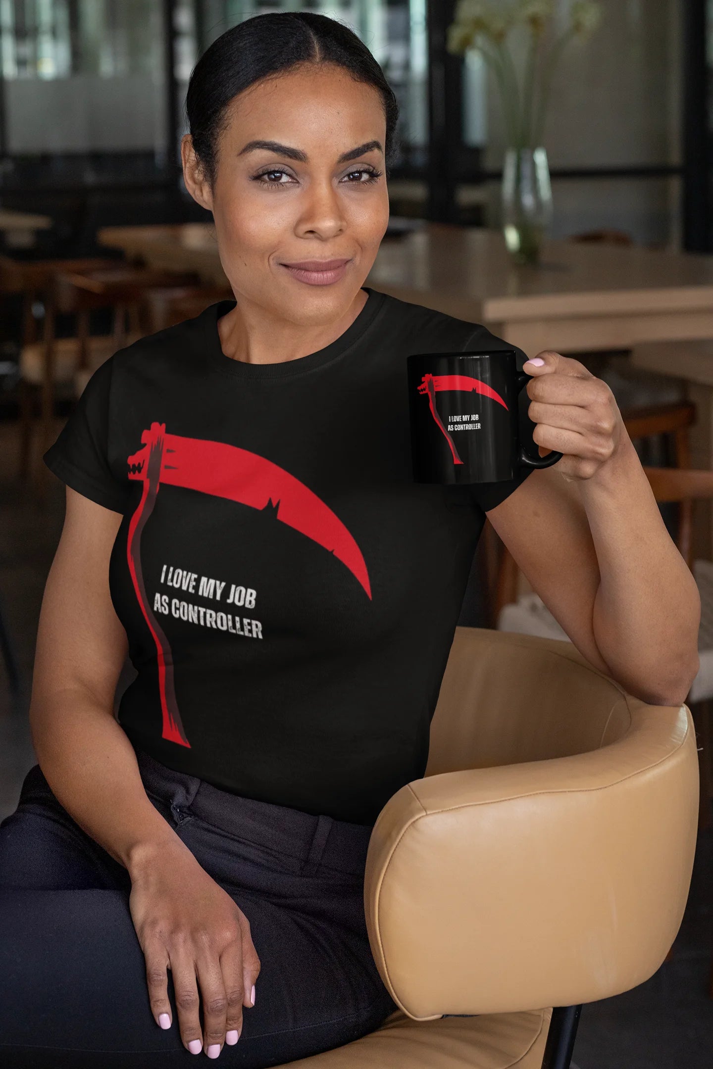 Woman wearing a black t-shirt with a red graphic and text, holding a black mug in a casual setting.