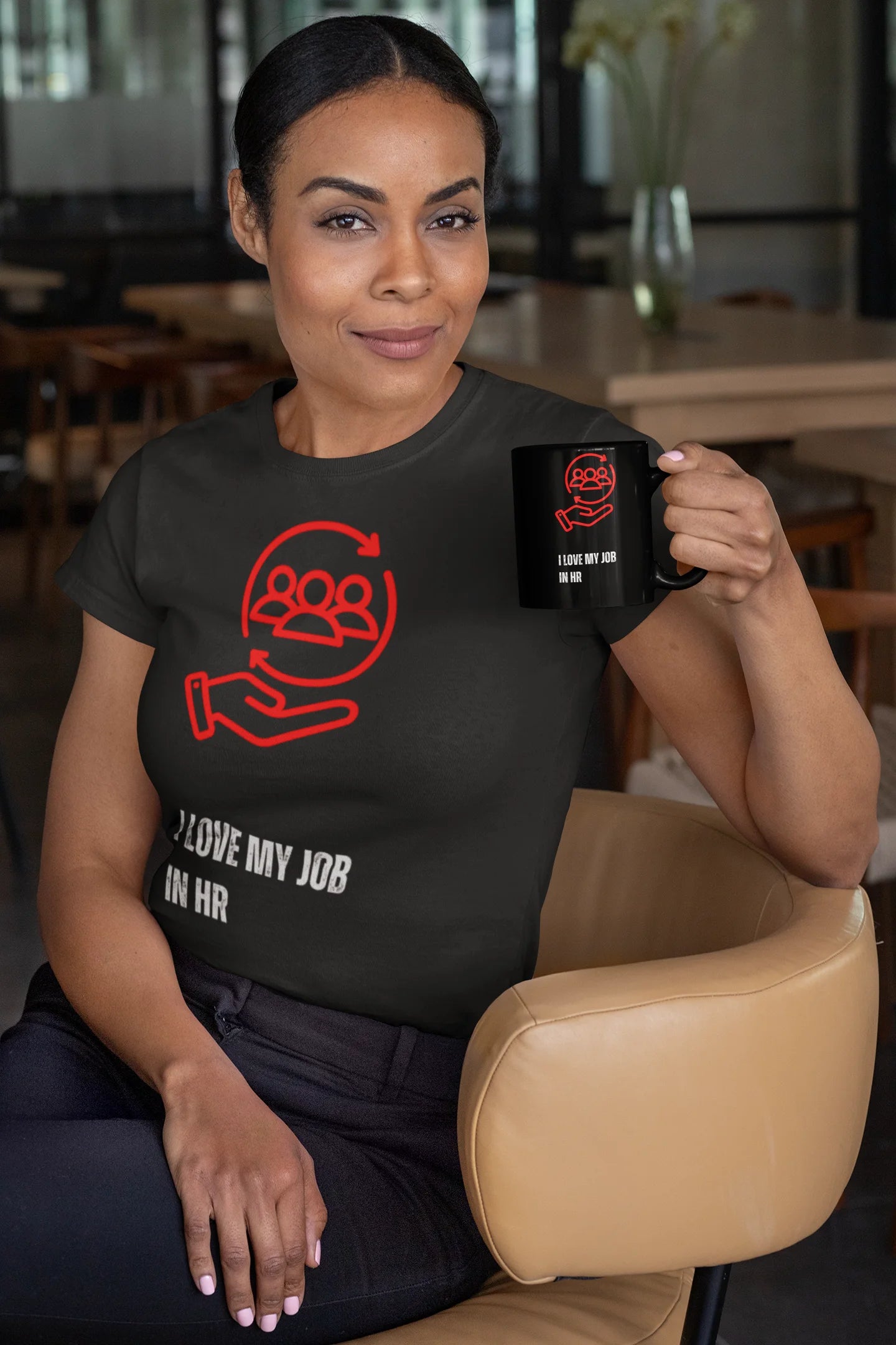 I love my Job T-Shirt Woman wearing a black t-shirt with a red graphic and text, holding a black mug in a casual setting.