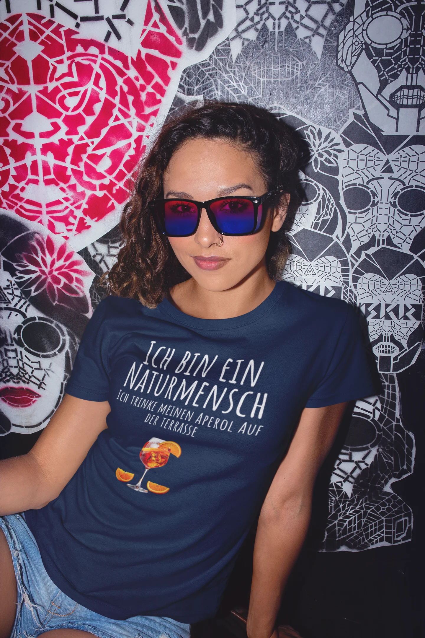 Person wearing a blue t-shirt with text and graphics, sitting against a colorful wall.