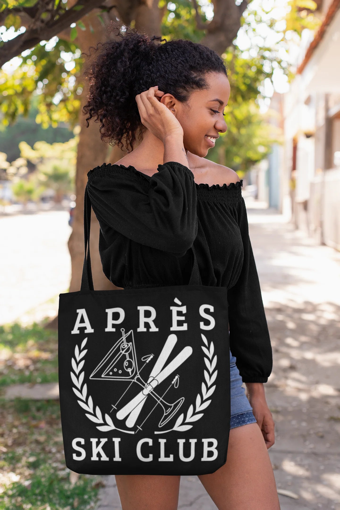 ski tote bag Woman holding a black tote bag with 'Ap
es Ski Club' design outdoors.