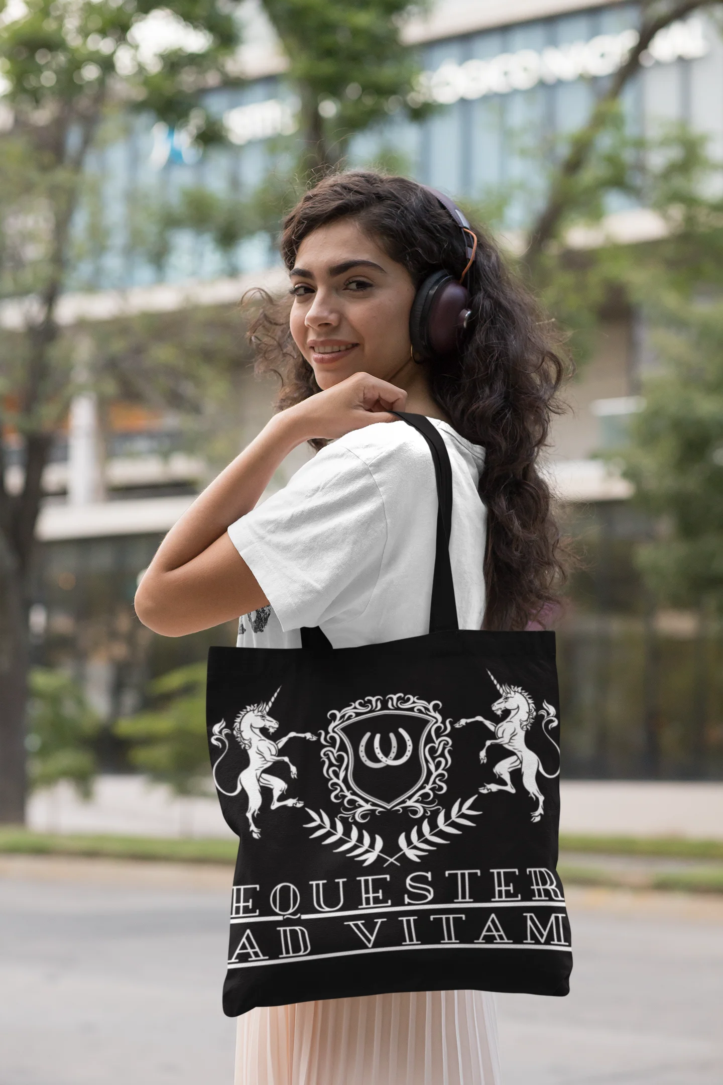 Woman wearing headphones and carrying a black tote bag with white designs and text.