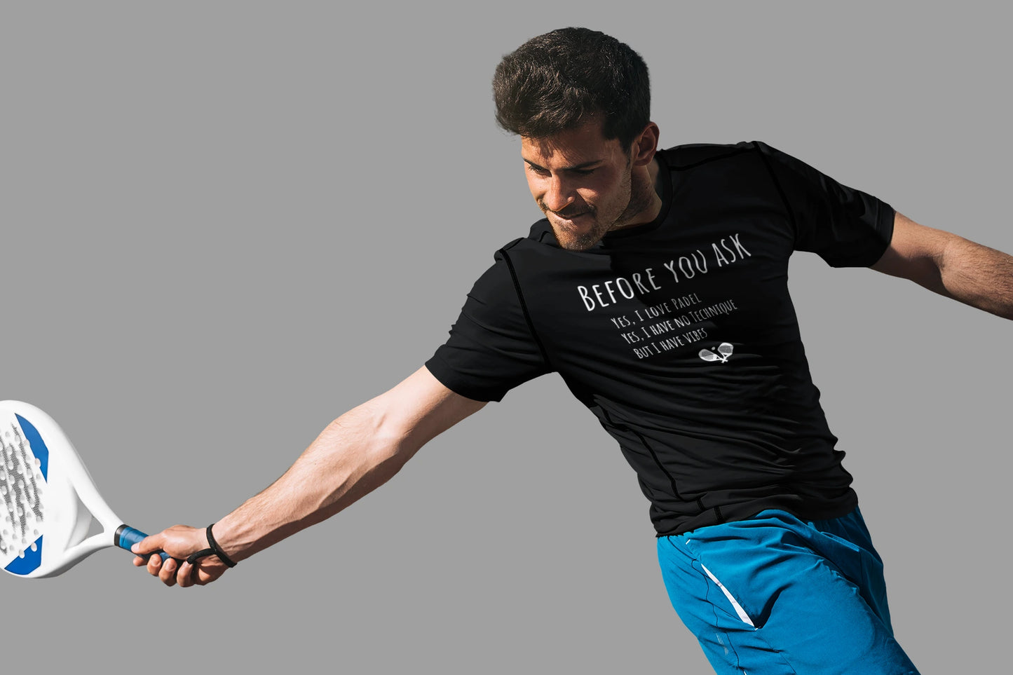 Man playing paddle tennis wearing a black t-shirt with text and blue shorts on a gray background